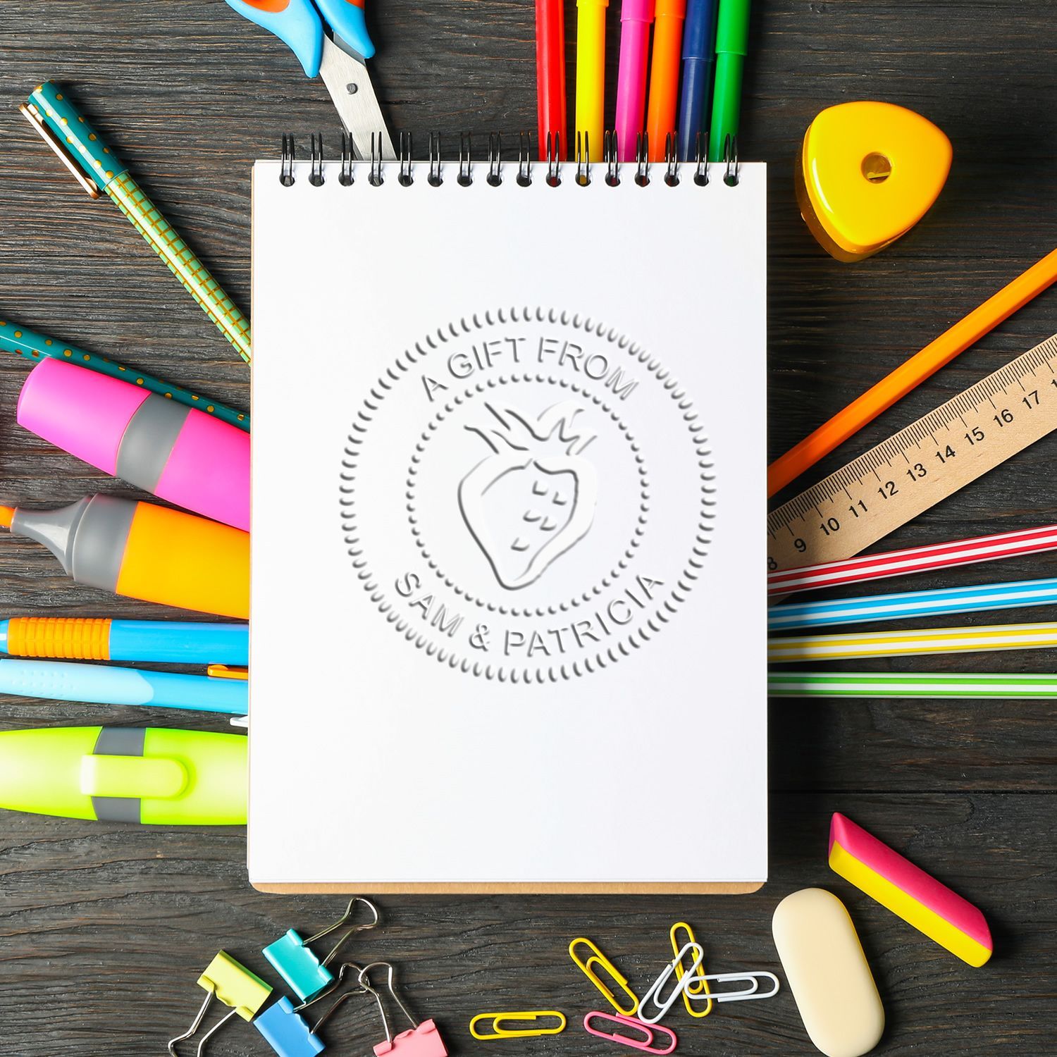 Colorful school stationery items ?????? blank spiral notebook with strawberry gift stamp on dark wooden desk.