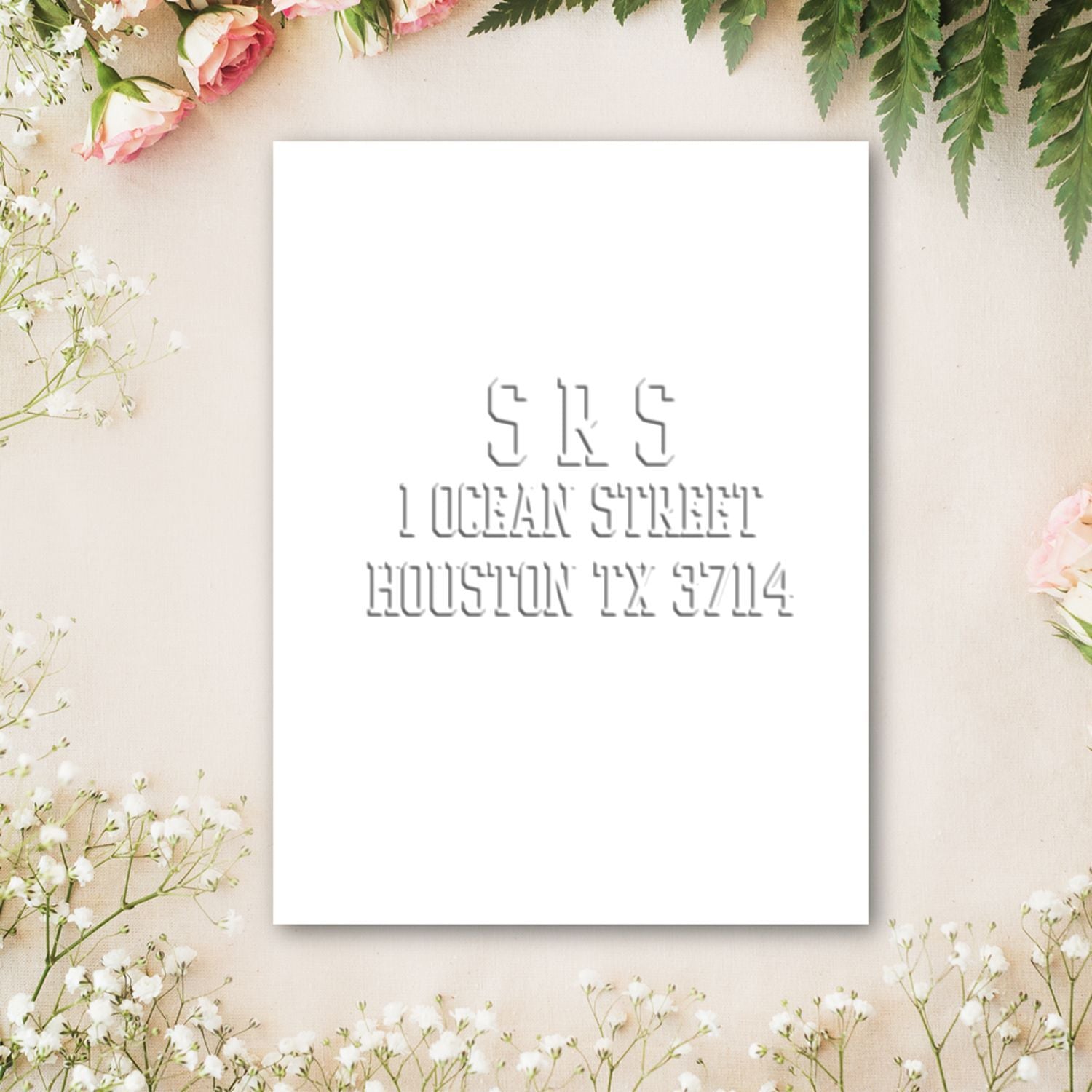 Floral wedding invitation card mockup with pink roses, greenery, and minimalist white stationery on a beige background.