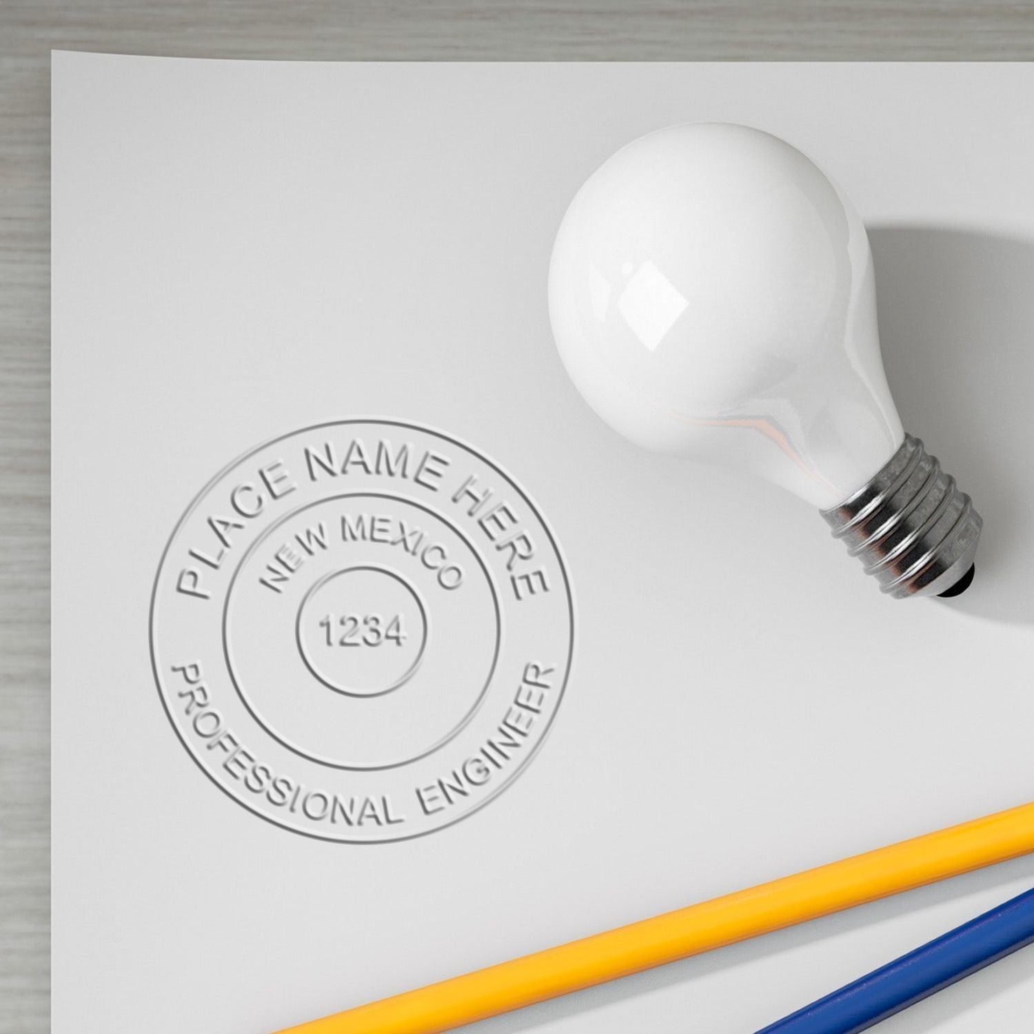 Custom New Mexico Professional Engineer seal stamp with light bulb on white paper and colored pencils