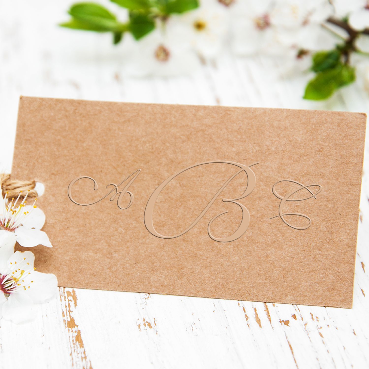 Rustic kraft paper card with Be lettering, white blossoms, and green leaves on a white wooden background