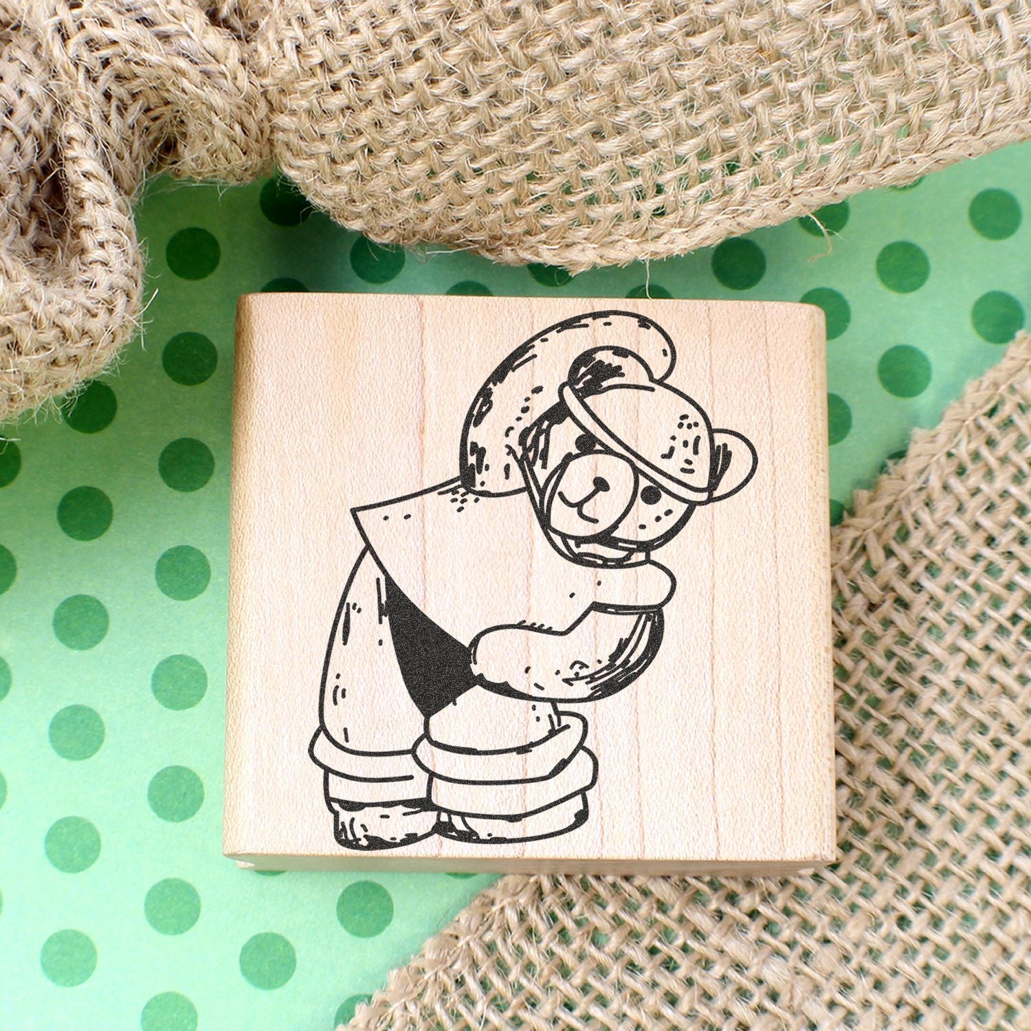 Wooden teddy bear stamp with cute black line art on green polka dot background and burlap fabric