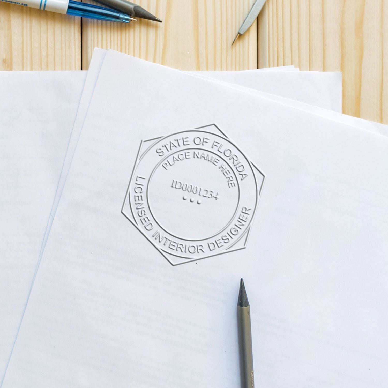 State of Florida licensed interior designer stamp on paperwork with pencils on a wooden desk.