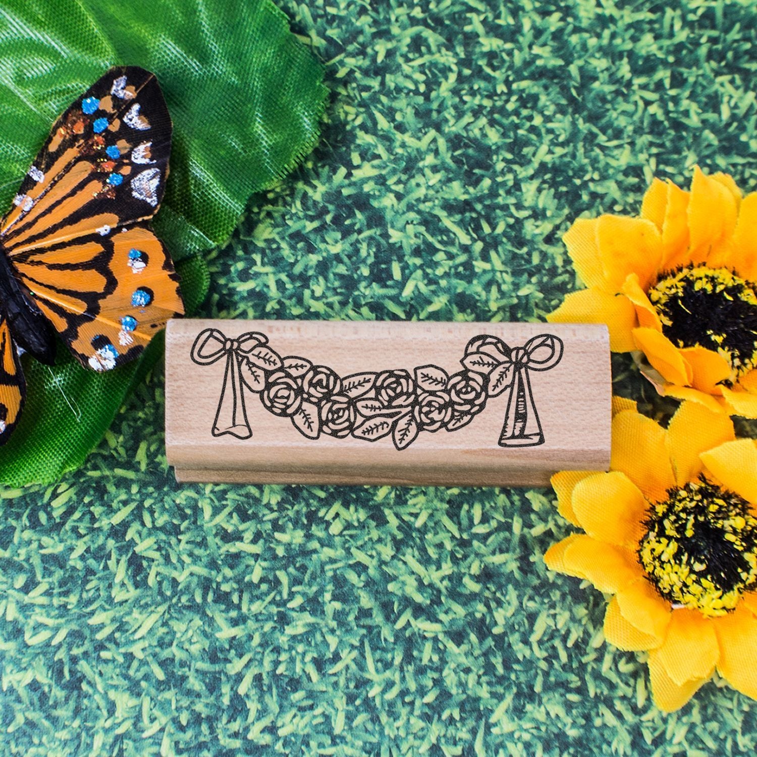 Decorative floral wooden stamp with butterfly and sunflowers on a green textured background.