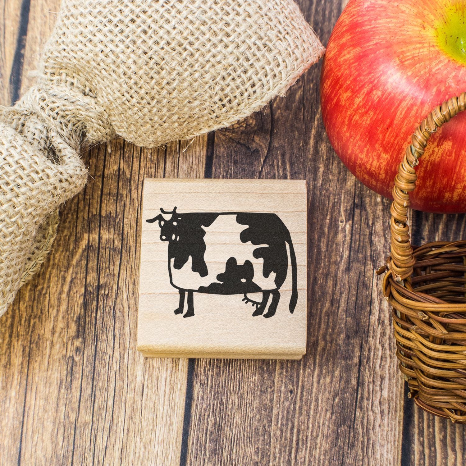 Cow silhouette rubber stamp on rustic wood with burlap sack, apple, and wicker basket.