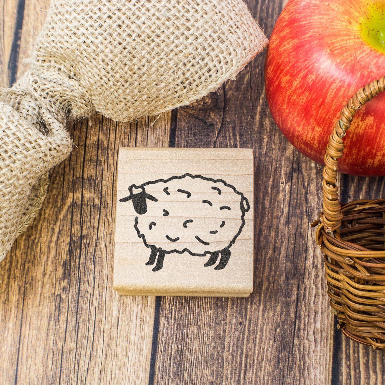Wooden sheep stamp with rustic farm decor, apple, and burlap on a wooden table