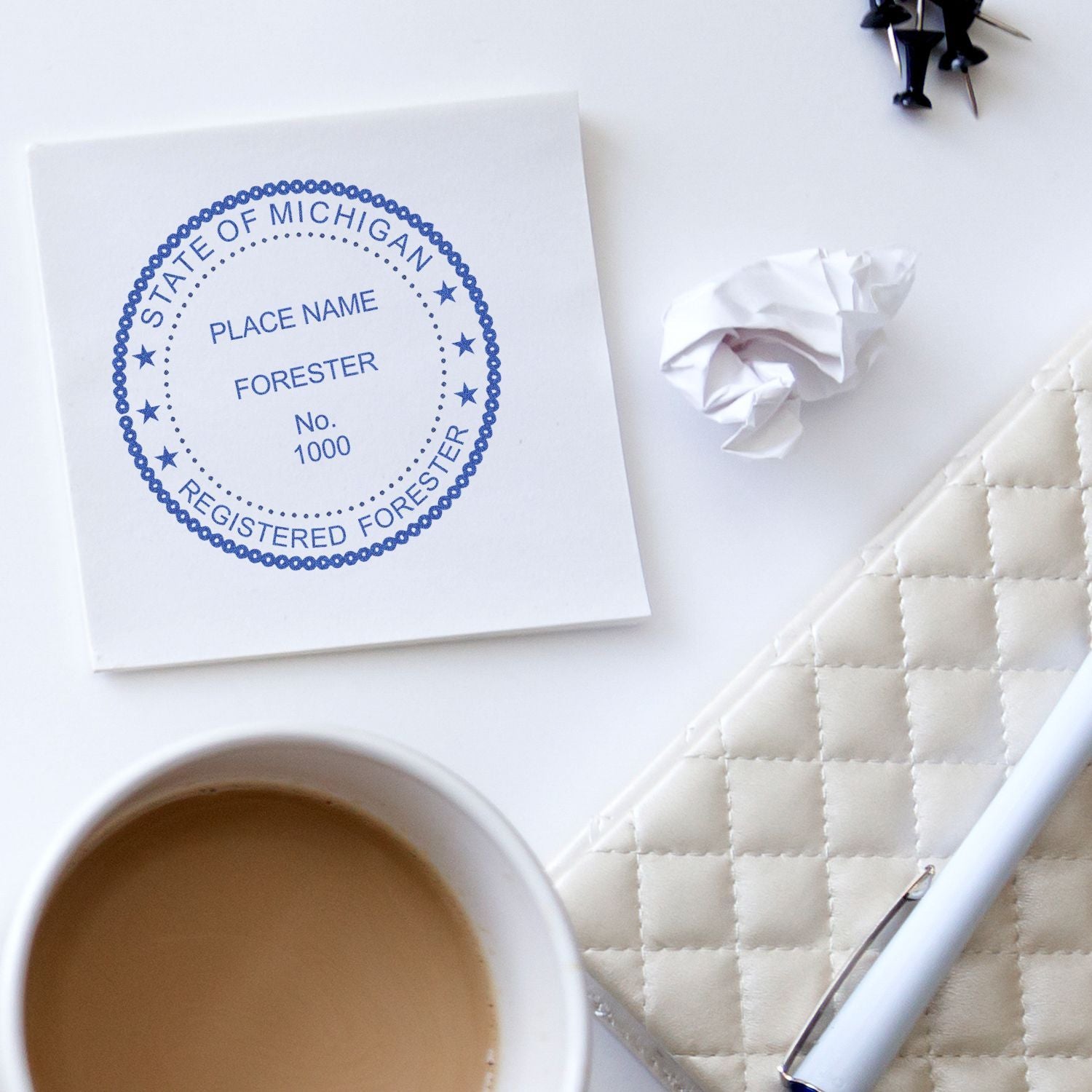 Michigan State Registered Forester certificate on a white desk with coffee cup, pen, notebook, and crumpled paper.