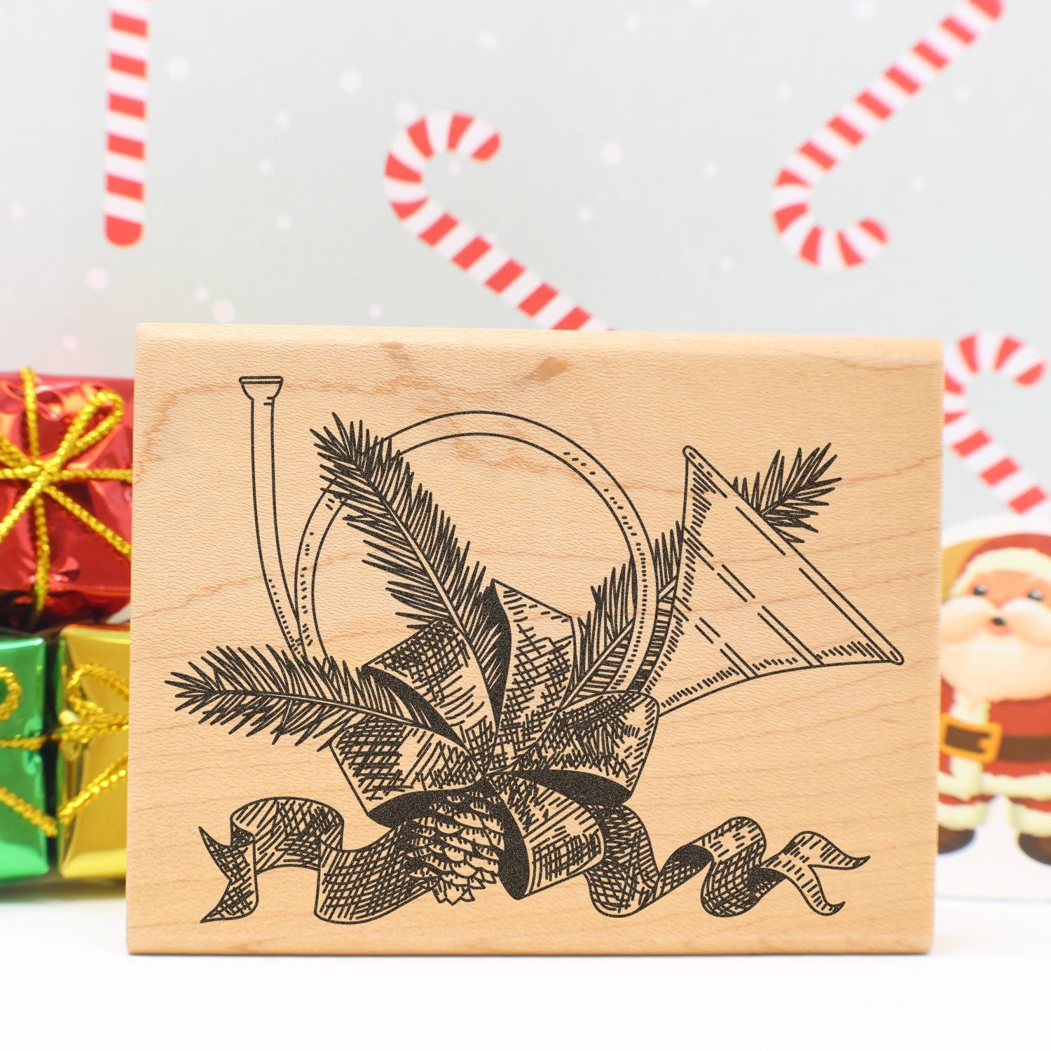 Rustic wooden Christmas gift with engraved festive pine and ribbon design, set against candy cane holiday decor and wrapped presents.
