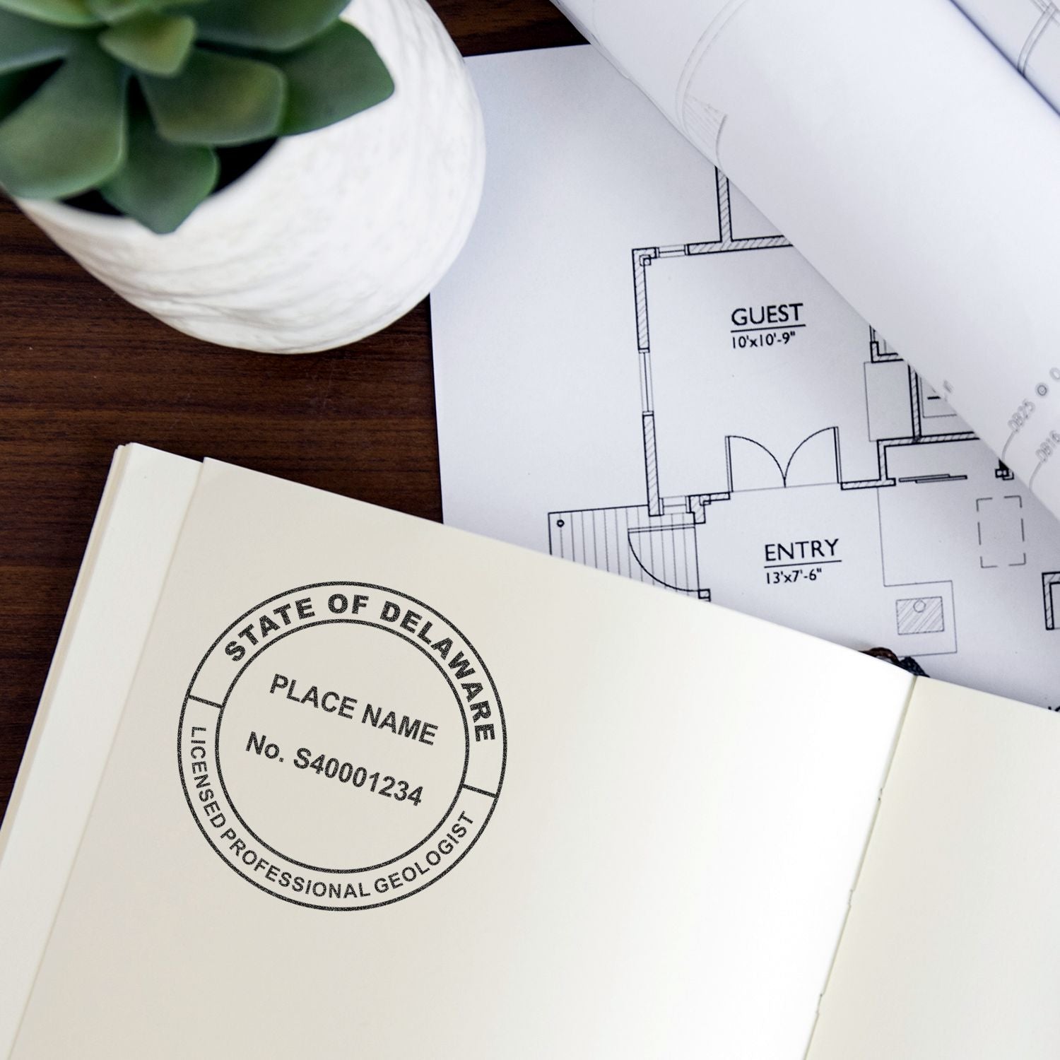 Architectural floor plan blueprint with Delaware licensed professional geologist stamp on notebook beside succulent plant.