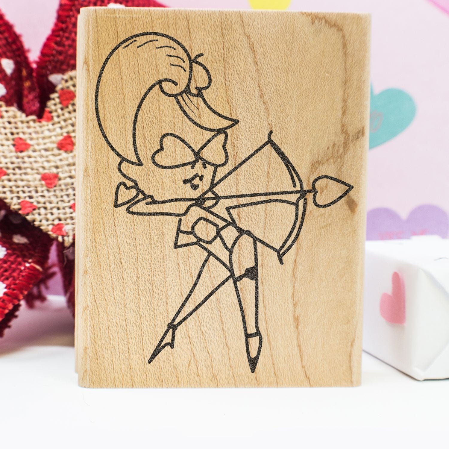 Wooden stamp with cute cupid angel holding a bow and arrow, engraved on a craft block with pastel heart background