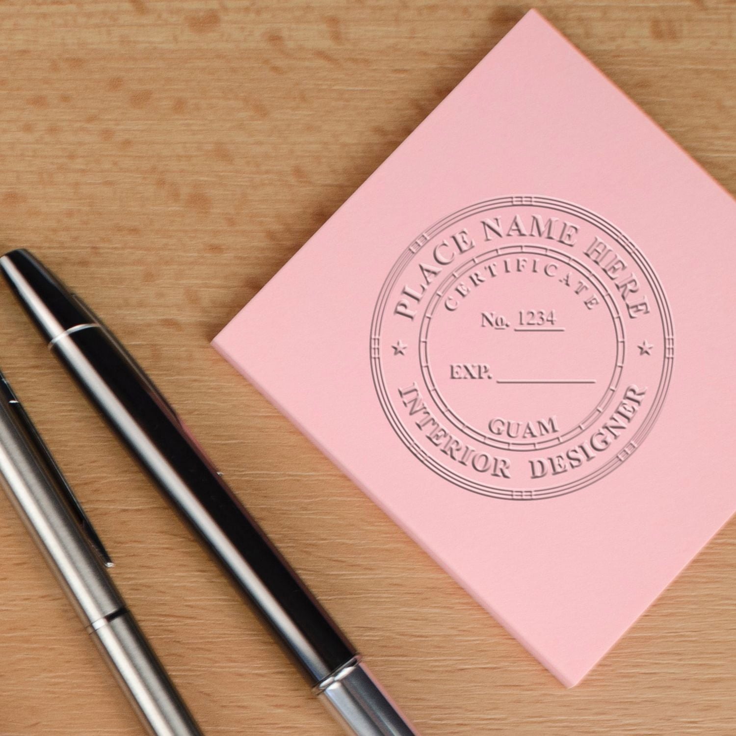 Pink customizable interior designer certificate booklet with pens on a wooden desk.