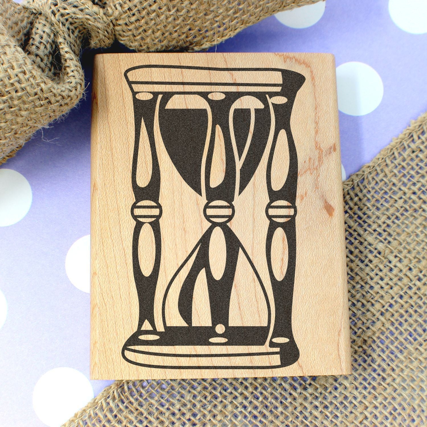 Wooden hourglass stamp on rustic burlap and purple polka dot background, close-up of handmade craft design