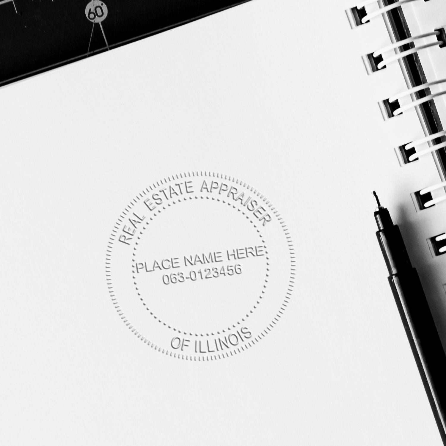 Black and white close-up of a Real Estate Appraiser of Illinois notebook page with embossed seal, spiral binding, and pen.