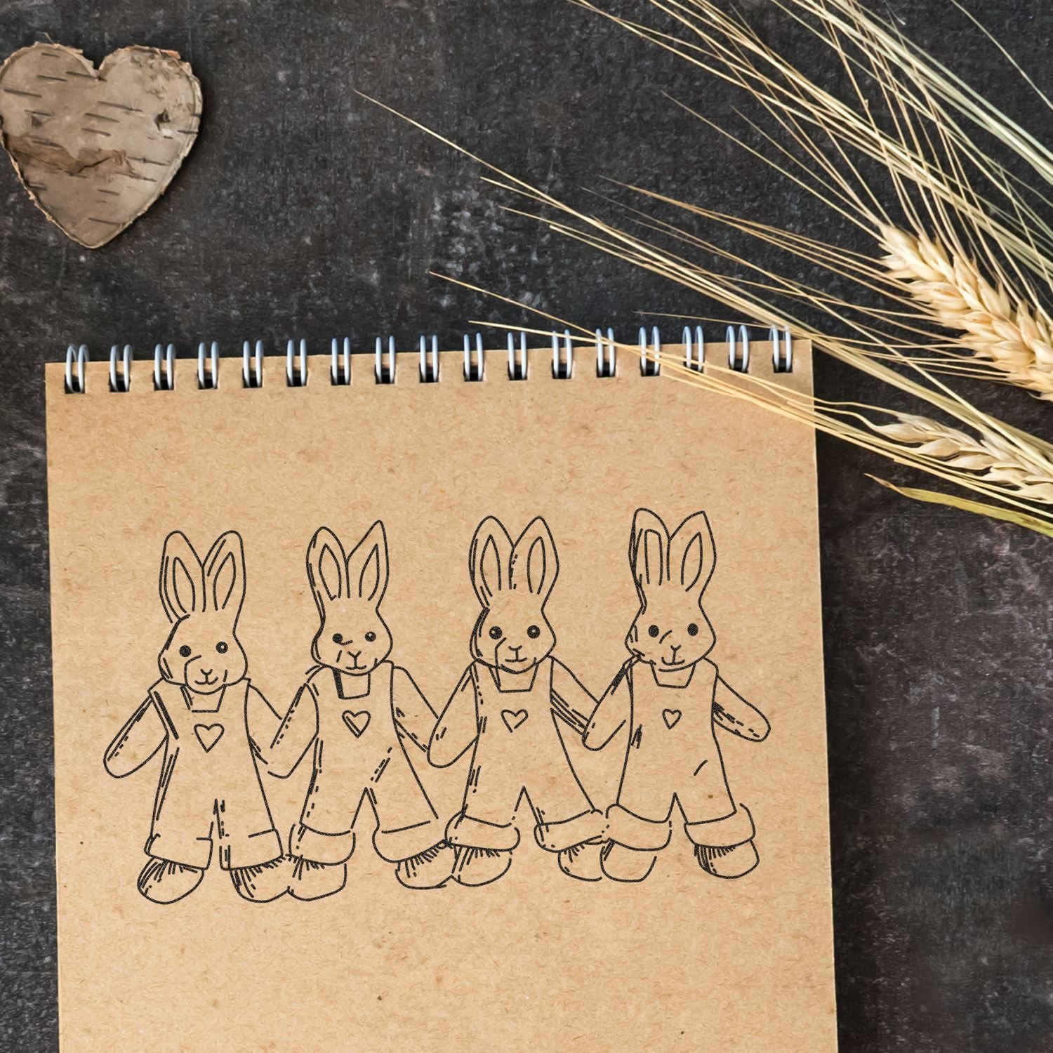 Cute rabbit illustration on a kraft notebook, styled with dried wheat and rustic heart decor on a dark background.