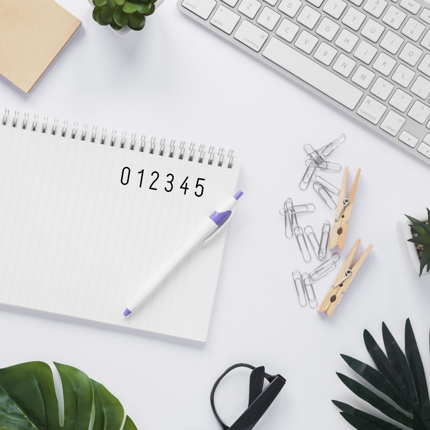 Minimal office workspace with open spiral notebook showing numbers 05 and a computer keyboard, supporting productivity planning.