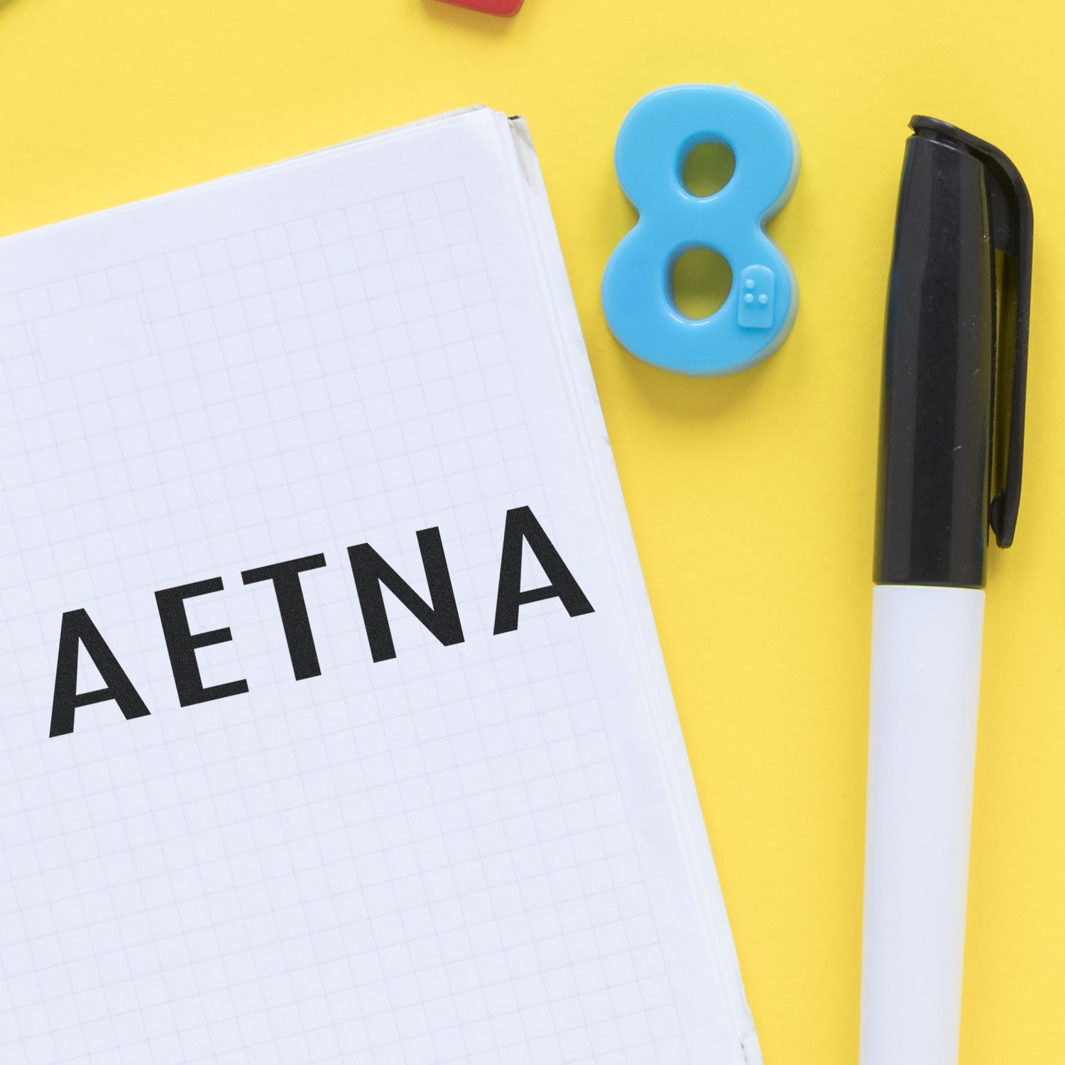 Aetna notebook with blue number 8 and pen on a yellow background.