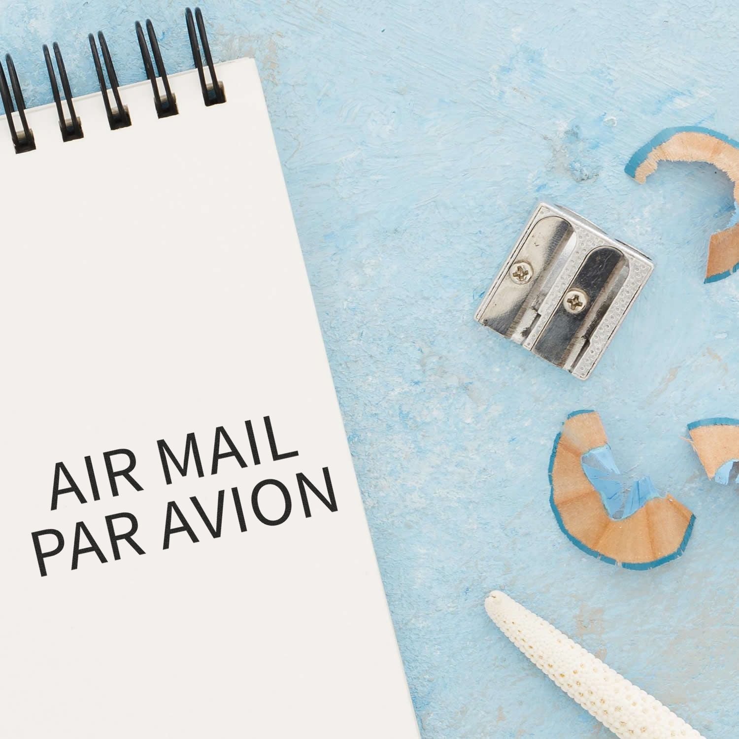 Air mail Par Avion postcard with metal binder clip and travel accessories on a blue background.