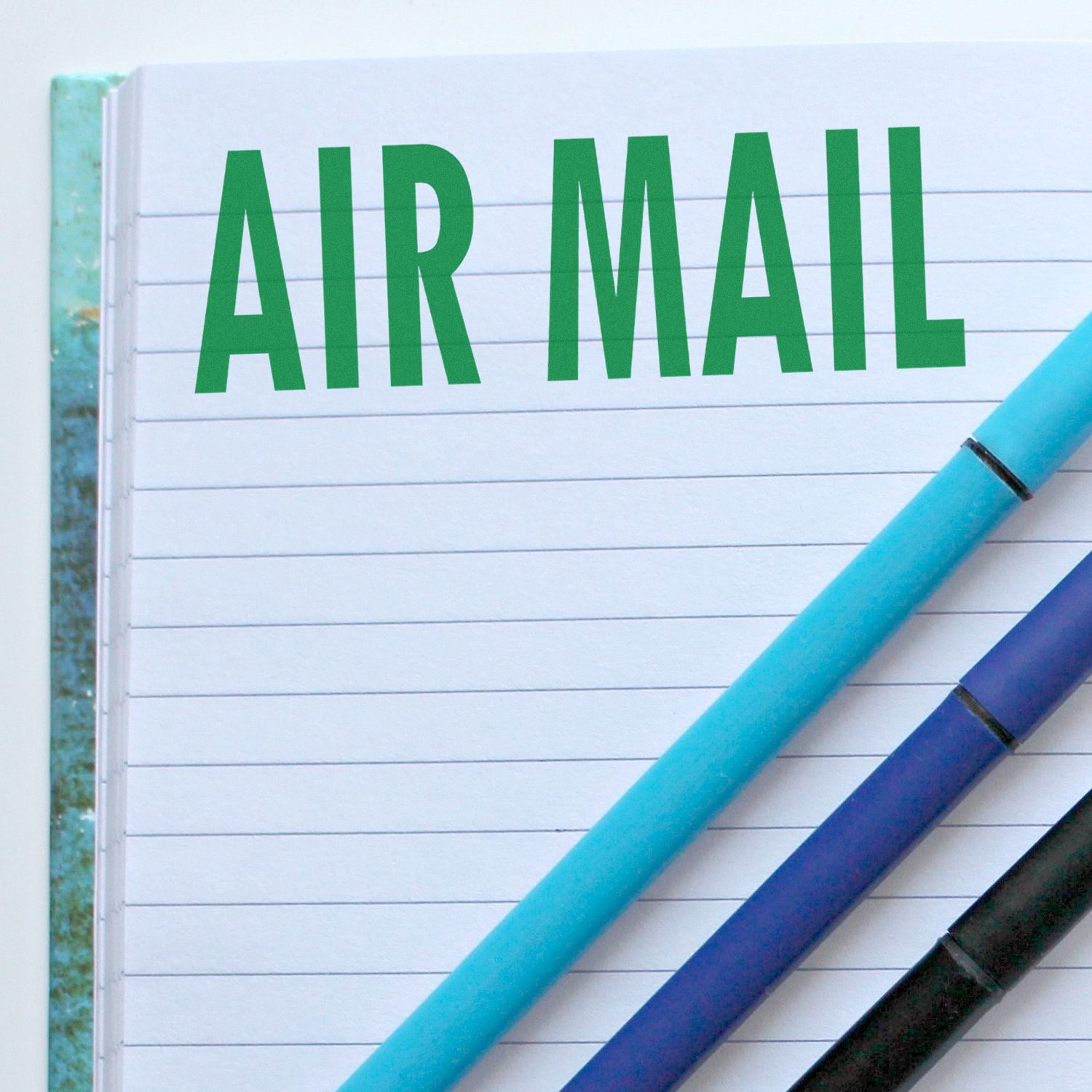 Air Mail text on lined notebook paper with pens, representing postal shipping and mail delivery services.