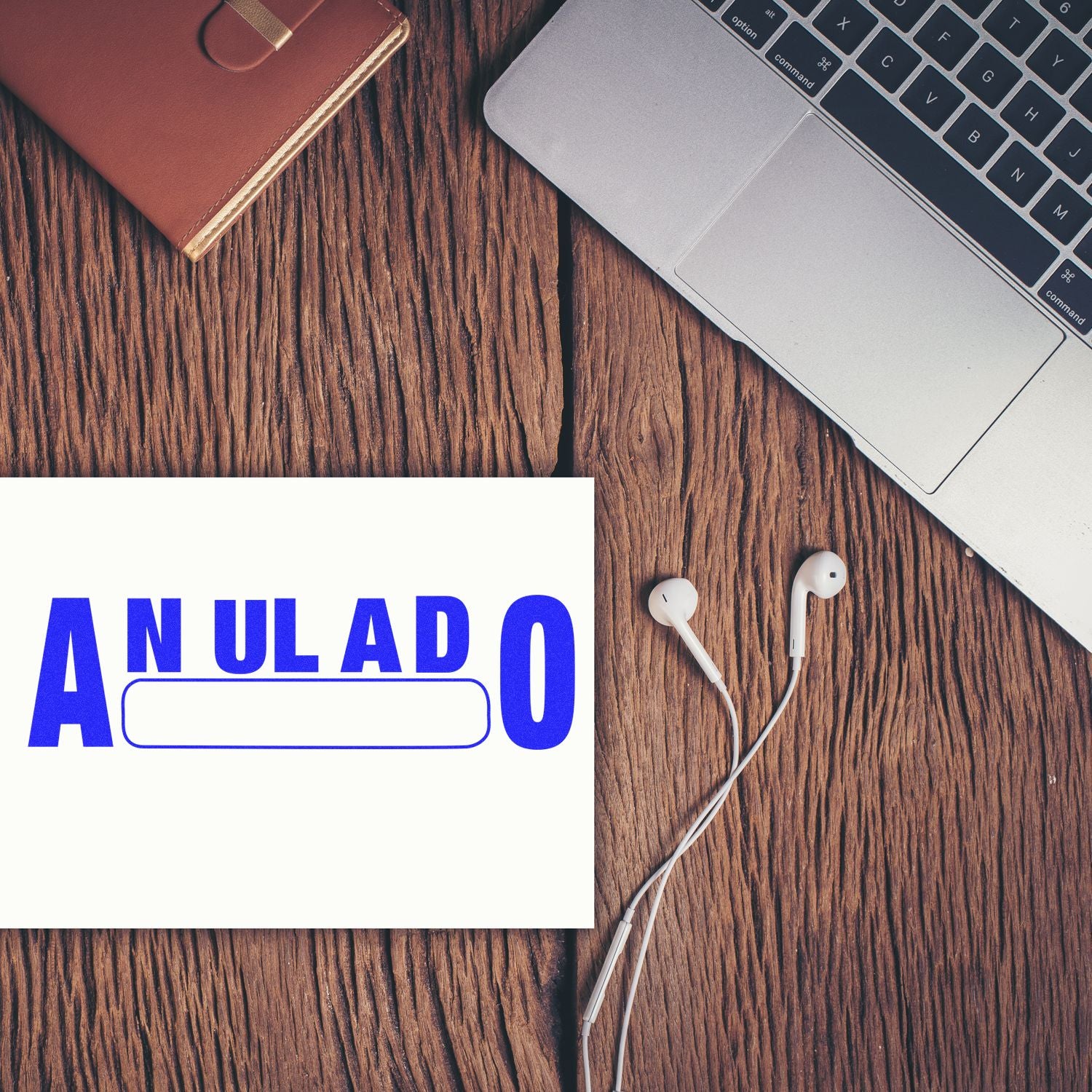 Laptop, earphones and notebook on a wooden desk with a sign reading ANULADO