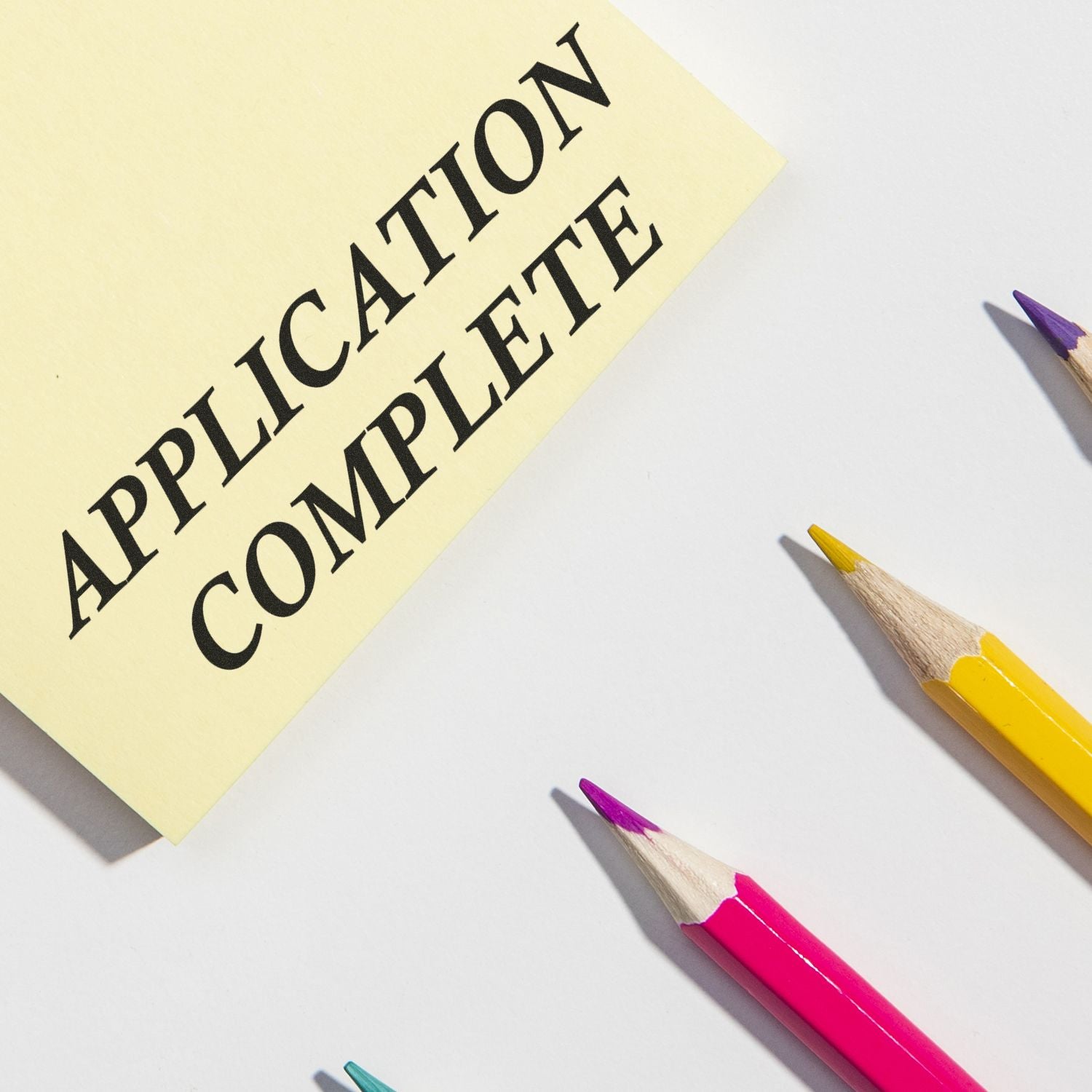 Application form message APPLICATION COMPLETE on yellow paper with colored pencils, promoting submitting complete job or school applications.