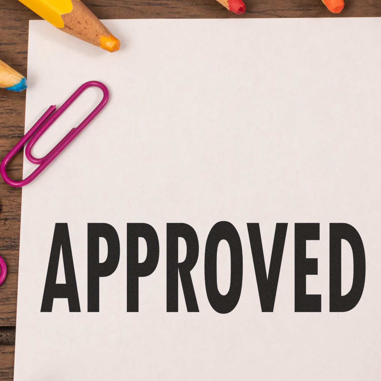 Approved paperwork concept with APPROVED text on paper, colored pencils and a purple paperclip during quality review for final approval on desk.