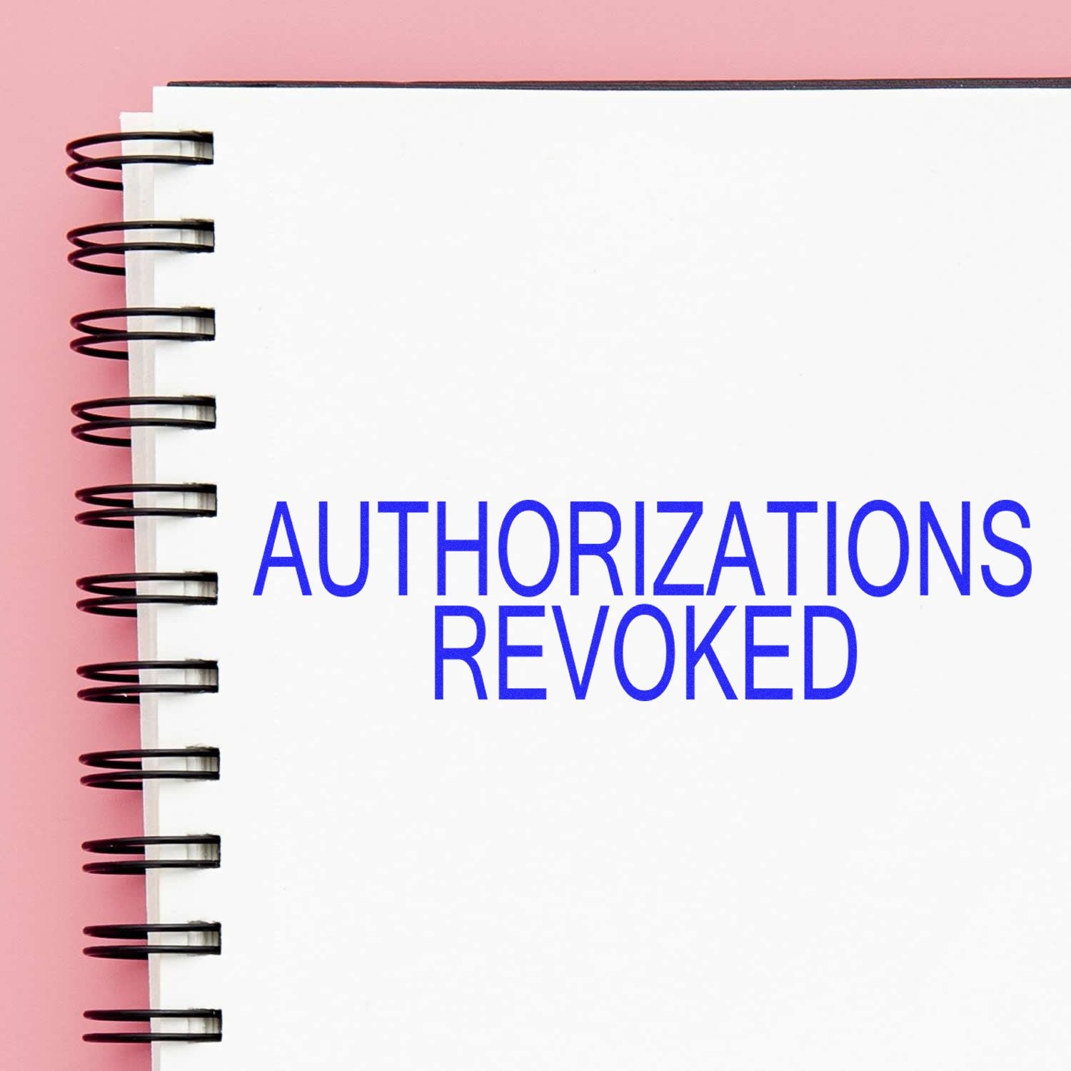 Close-up of spiral notebook with Authorizations Revoked text on pink background, legal and compliance concept.