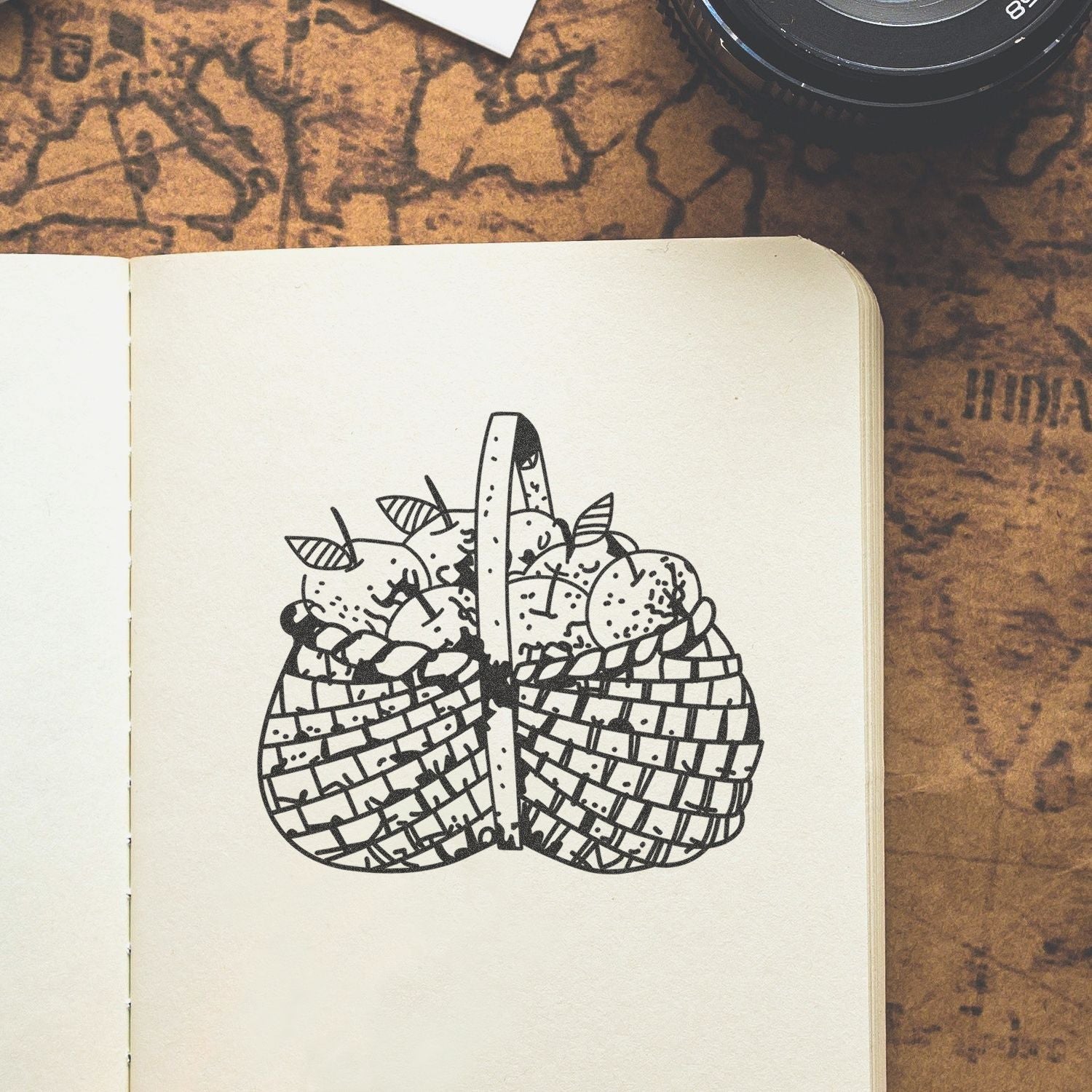 Open sketchbook with a black line drawing of a woven fruit basket on a vintage map-style background.