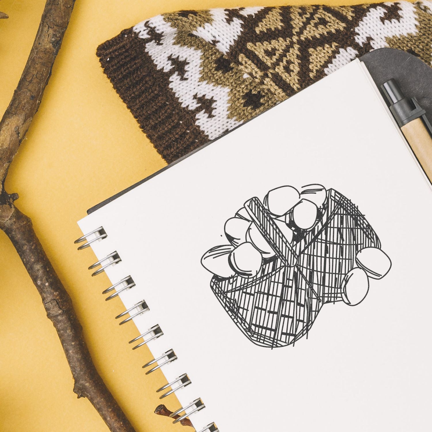 Sketchbook with abstract geometric flower illustration on a yellow background, with pen, knitted fabric, and natural wood accents.