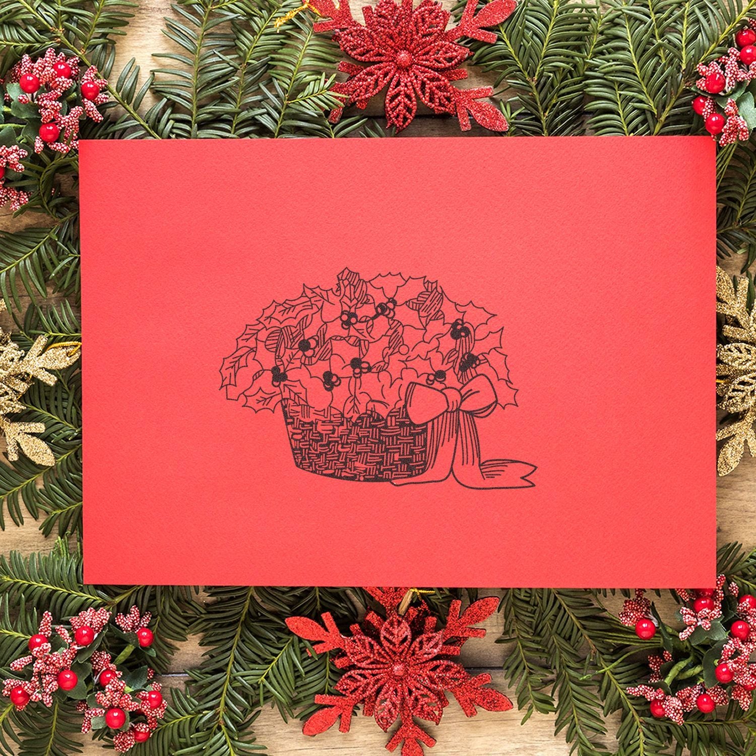 Festive red Christmas card with holly basket illustration surrounded by evergreen branches and holiday berries