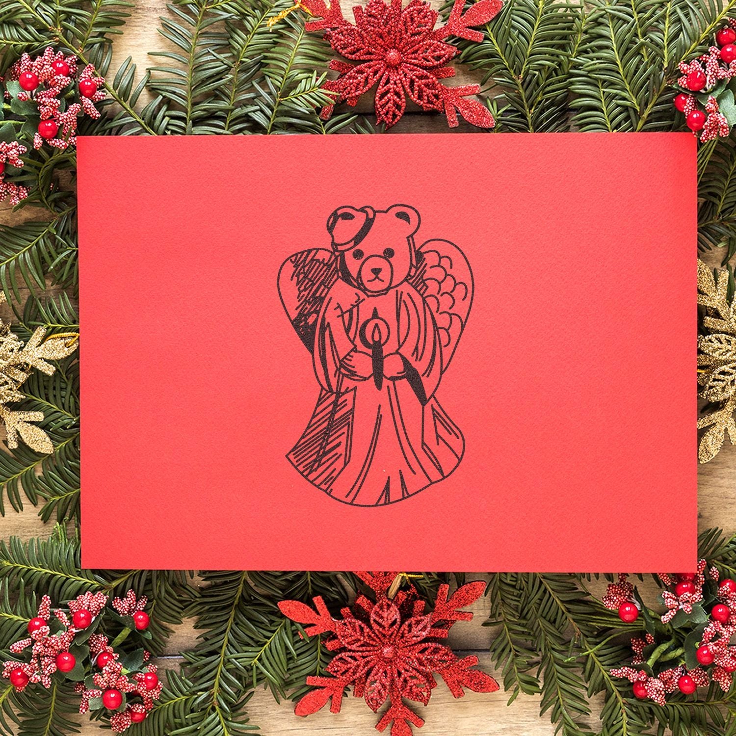 Red Christmas card with teddy bear angel holding a candle, surrounded by festive evergreen wreath and holiday decorations