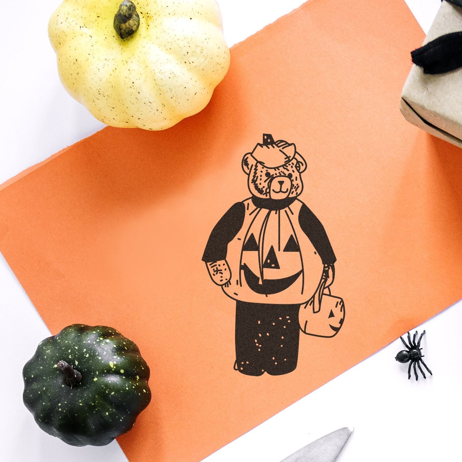 Halloween craft with orange paper, bear in a pumpkin costume, pumpkins, and a spooky spider decoration.