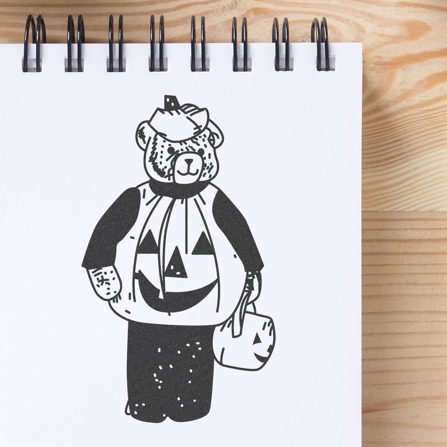 Black and white bear in a Halloween pumpkin costume on a spiral notebook on a wooden table.