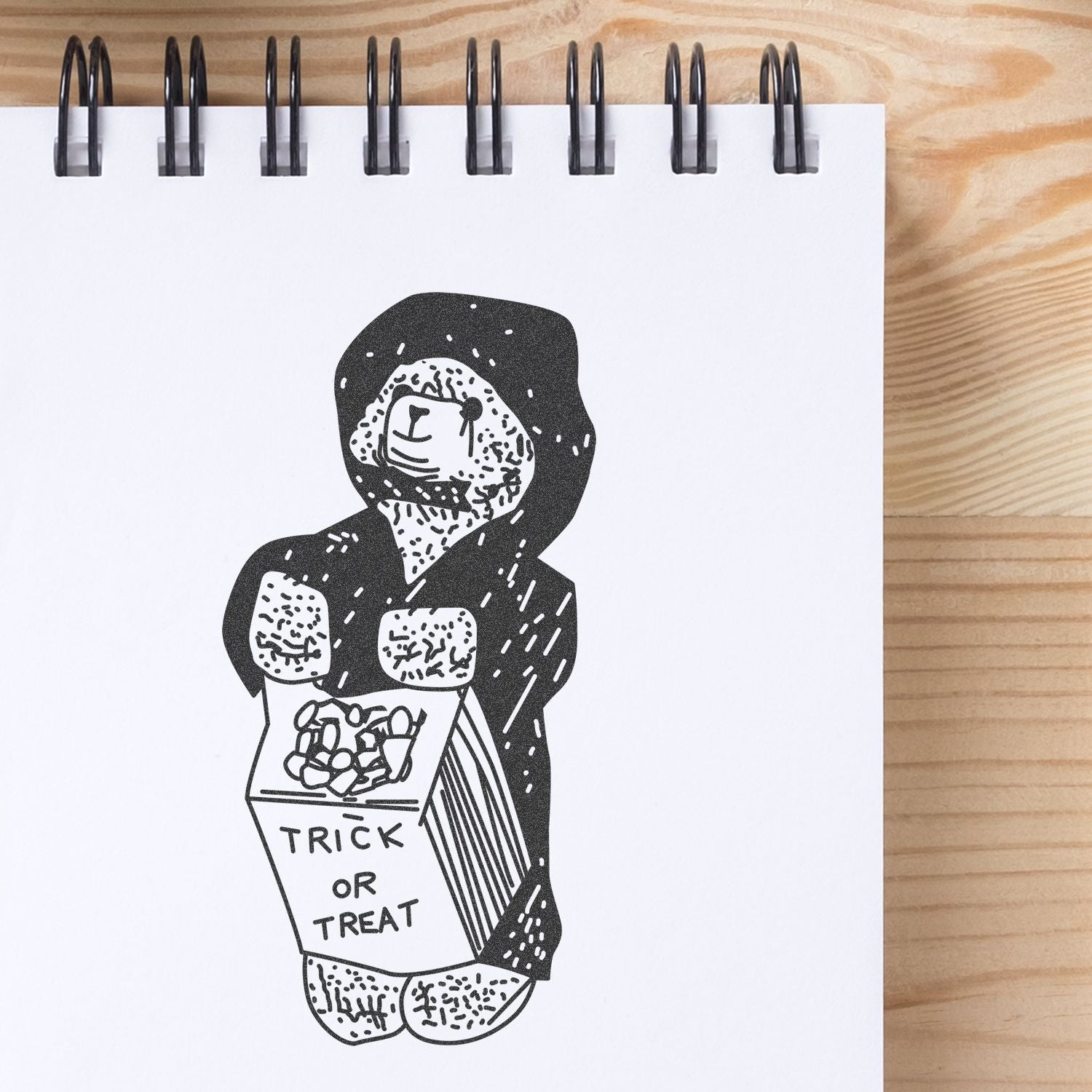 Black and white Halloween sketchbook illustration of a hooded trick-or-treat figure holding a candy box on a spiral notebook page.