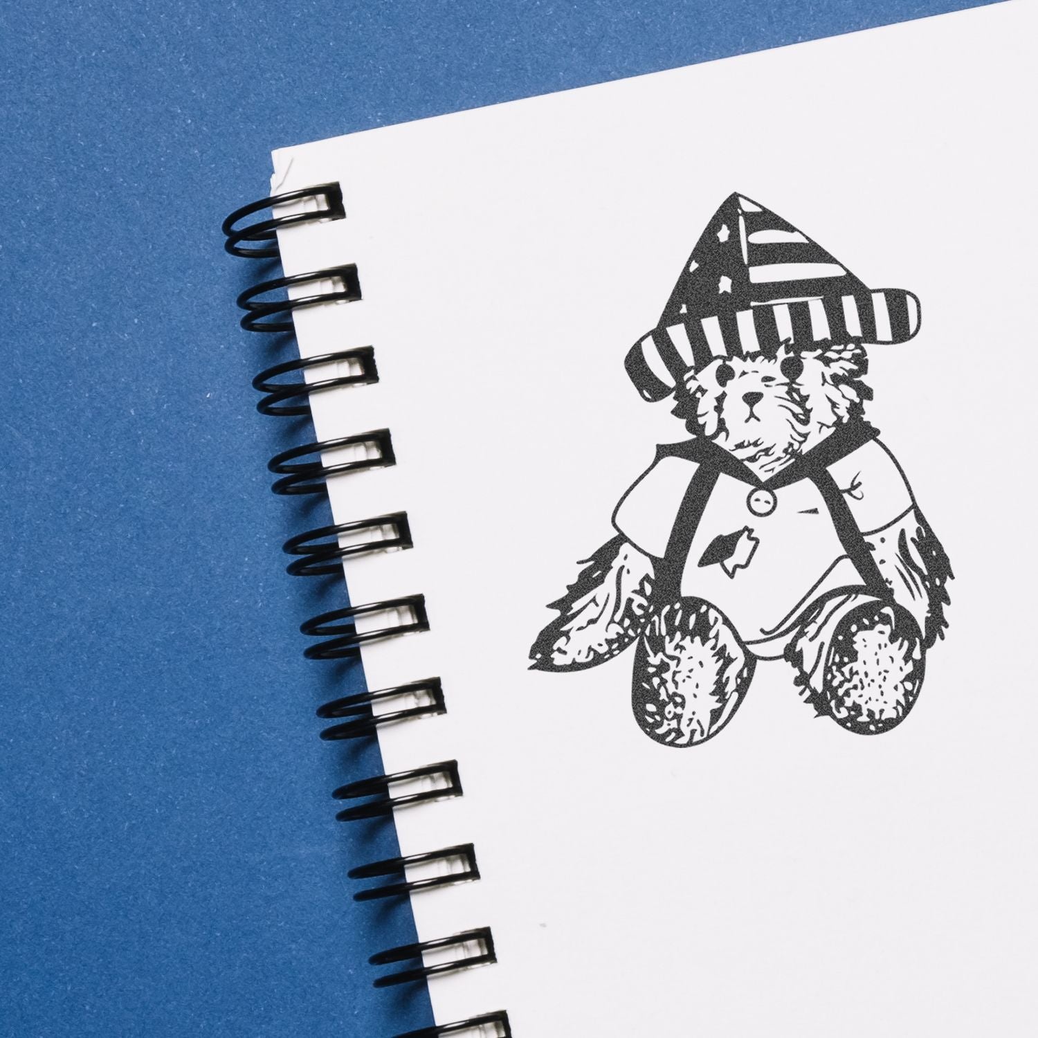 Teddy bear illustration in a spiral notebook on a blue background, cute hand-drawn art concept.