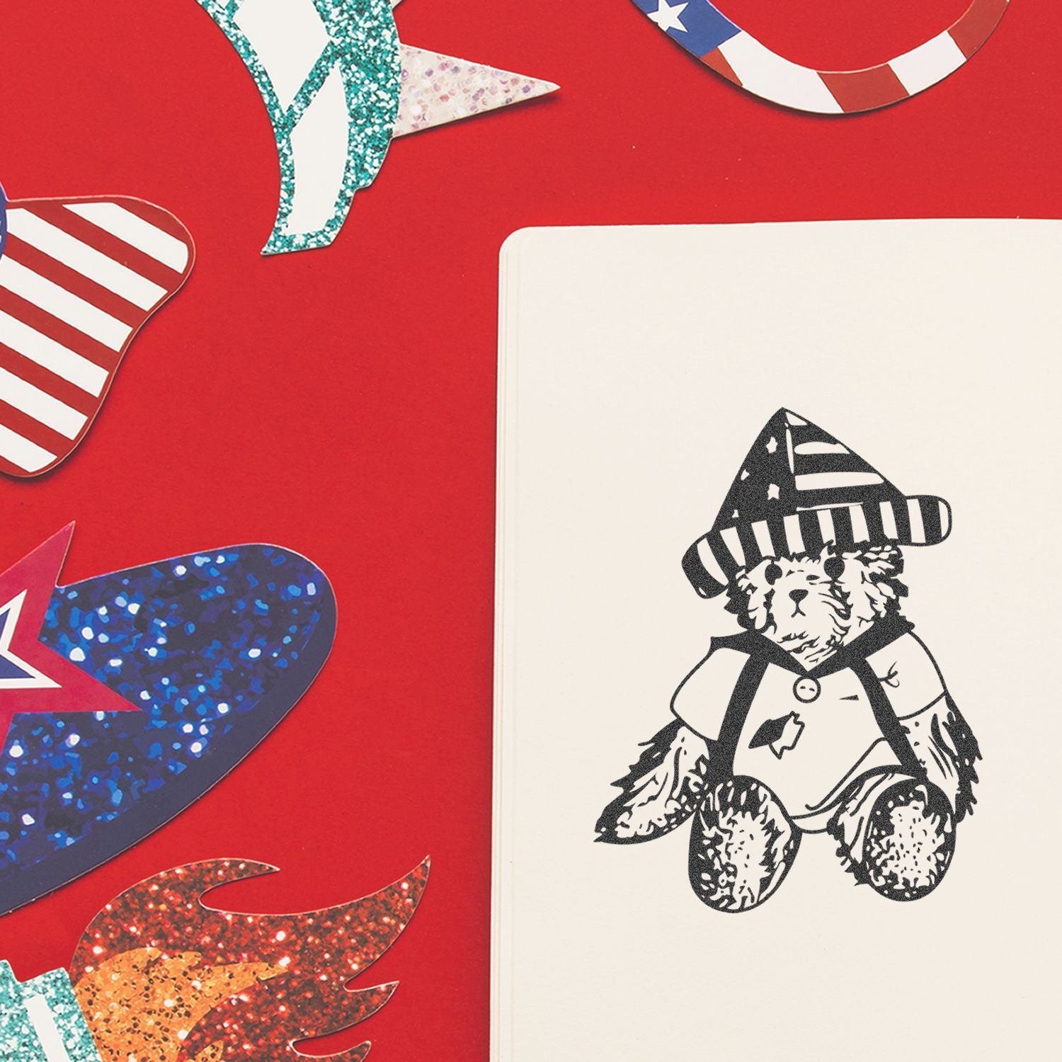 Patriotic scrapbook layout with glitter star cutouts and a teddy bear in a stars and stripes hat on a red background.