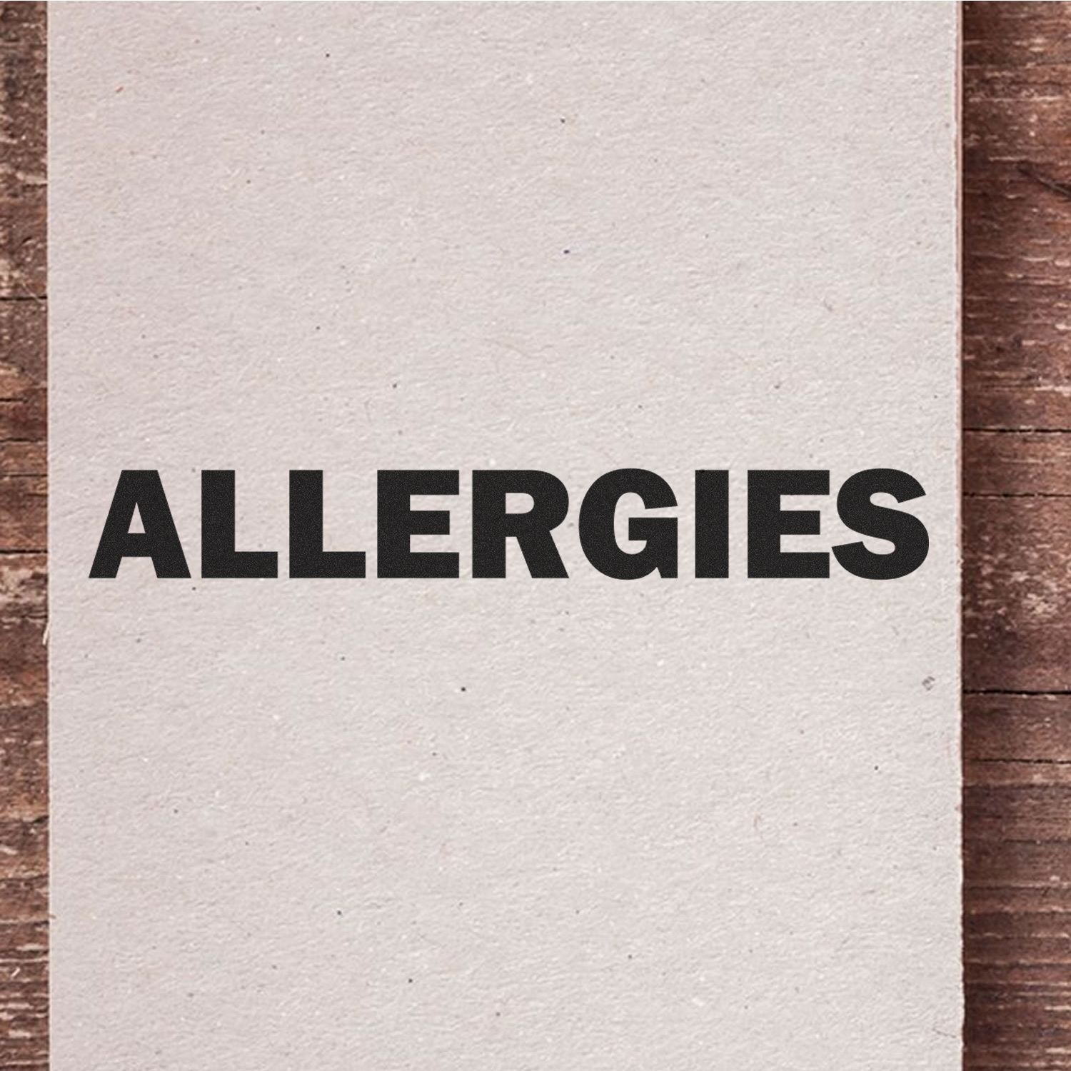 Close-up of a blank paper card with bold black ALLERGIES text on a rustic wooden background.