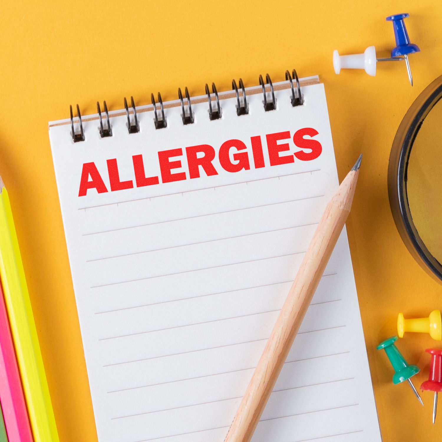 Allergies note on spiral notebook with pencil and push pins on yellow background