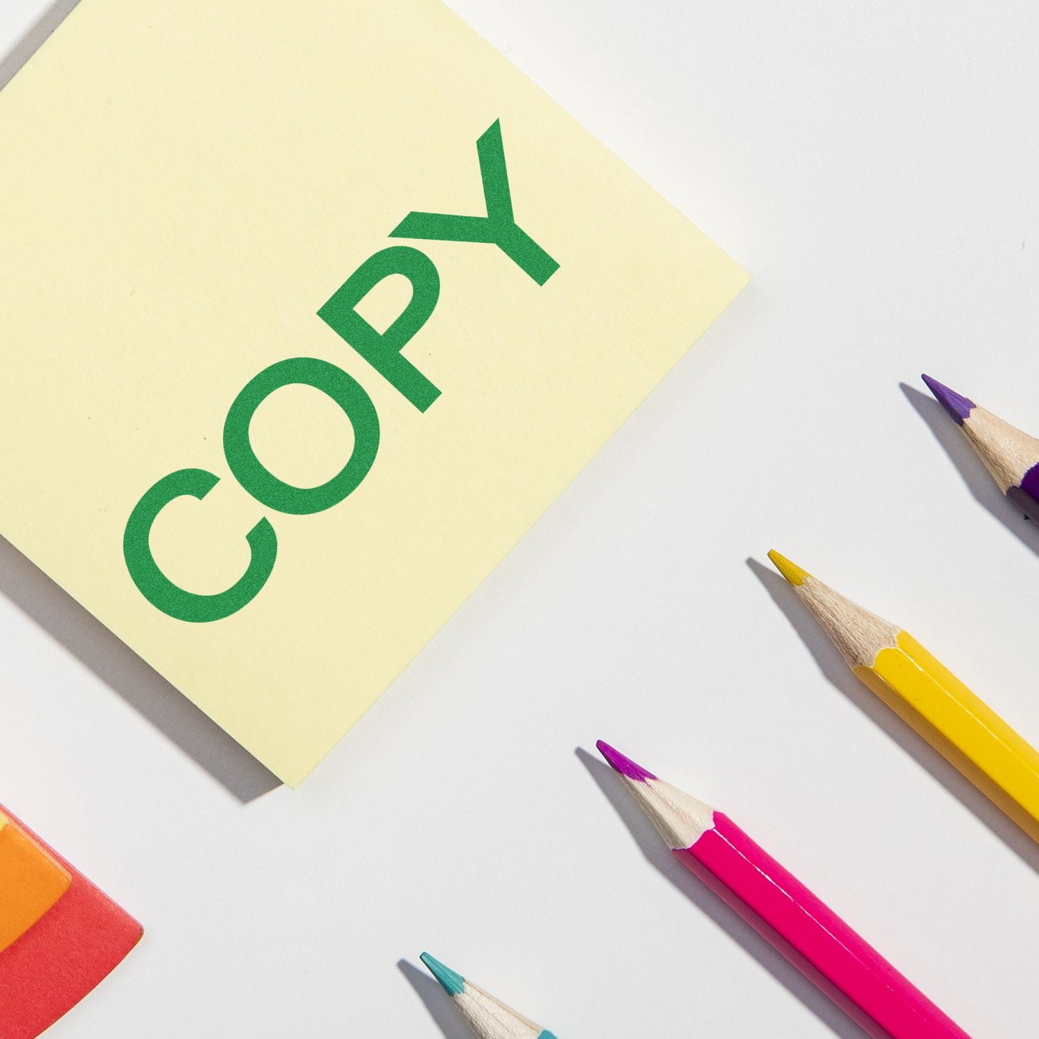 Green recycling symbol on yellow sticky note beside colored pencils, illustrating eco-friendly learning and sustainability for kids.
