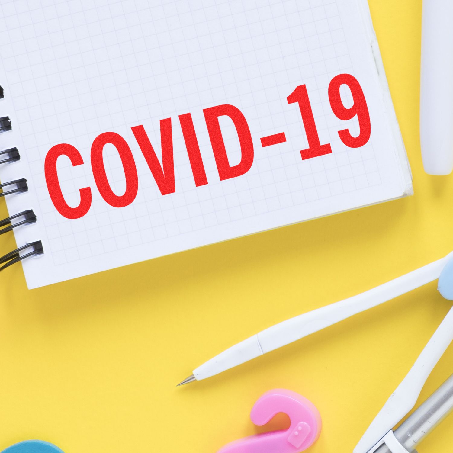 COVID-19 awareness notebook page with bold red COVID-19 text on grid paper and school supplies on yellow background