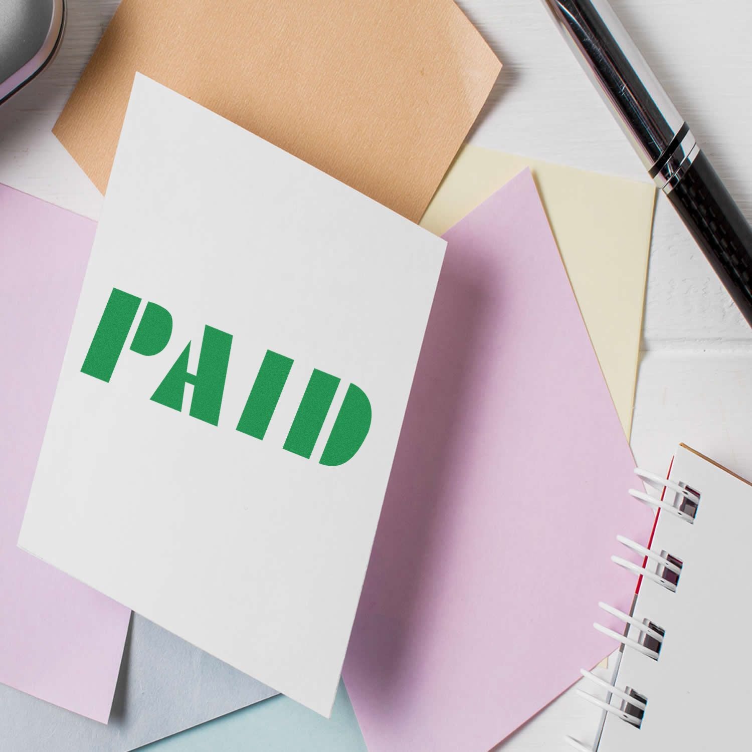 Colorful stationery with a white card labeled PAID, office supplies, and pastel paper sheets on a desk.
