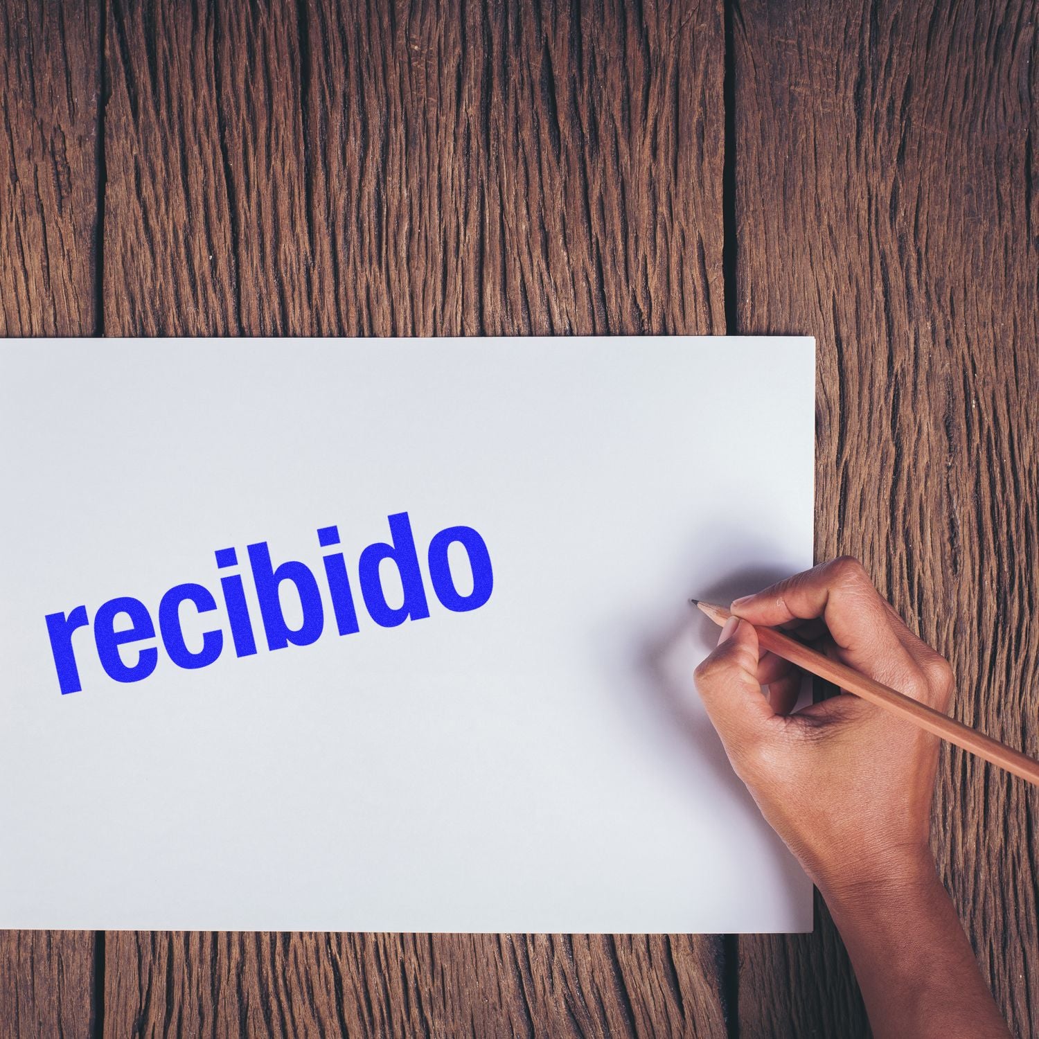 Man hand writes Recibido on paper with pencil over a wooden background, symbolizing document reception and confirmation