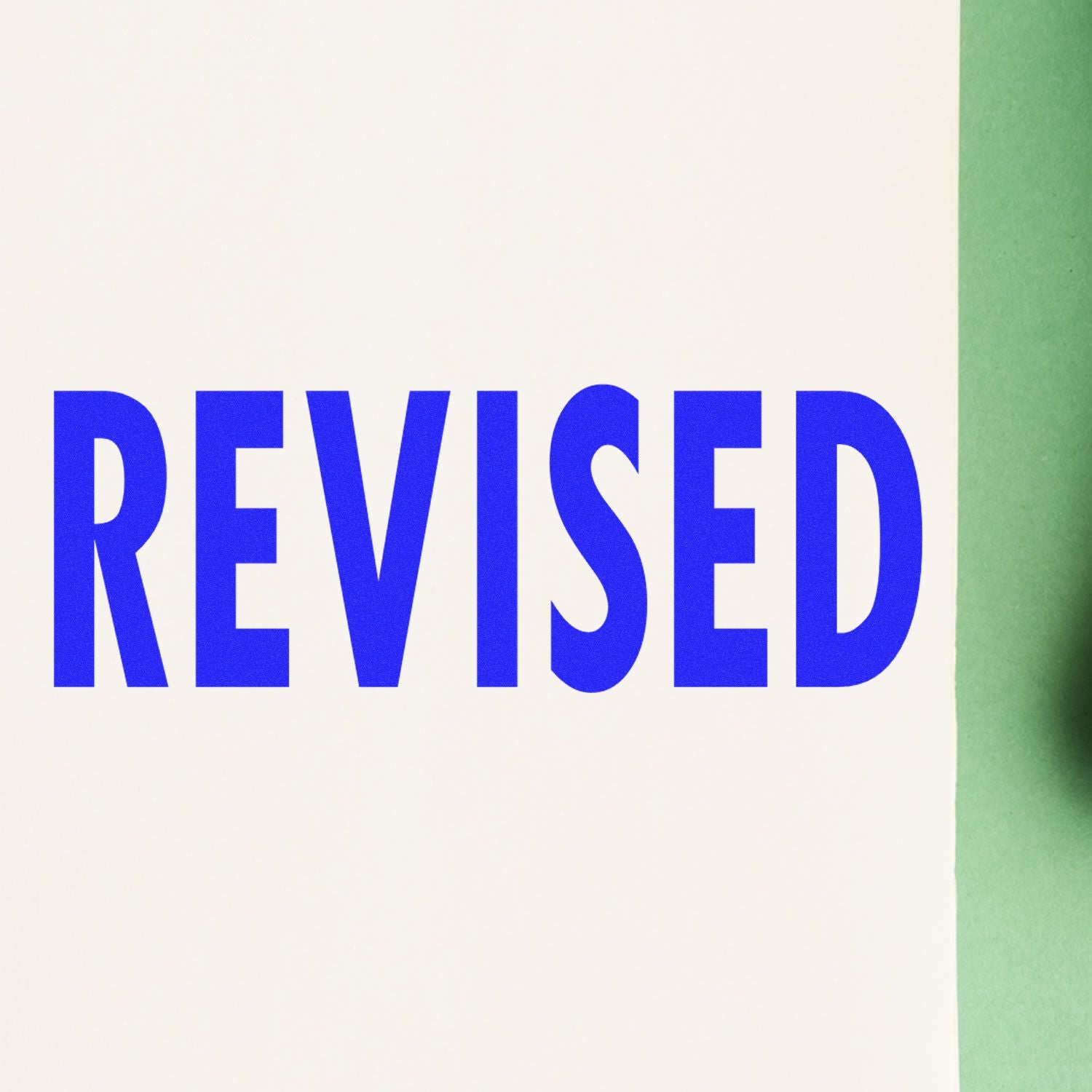 Blue REVISED text on white paper with green edge, close-up editorial document mark.