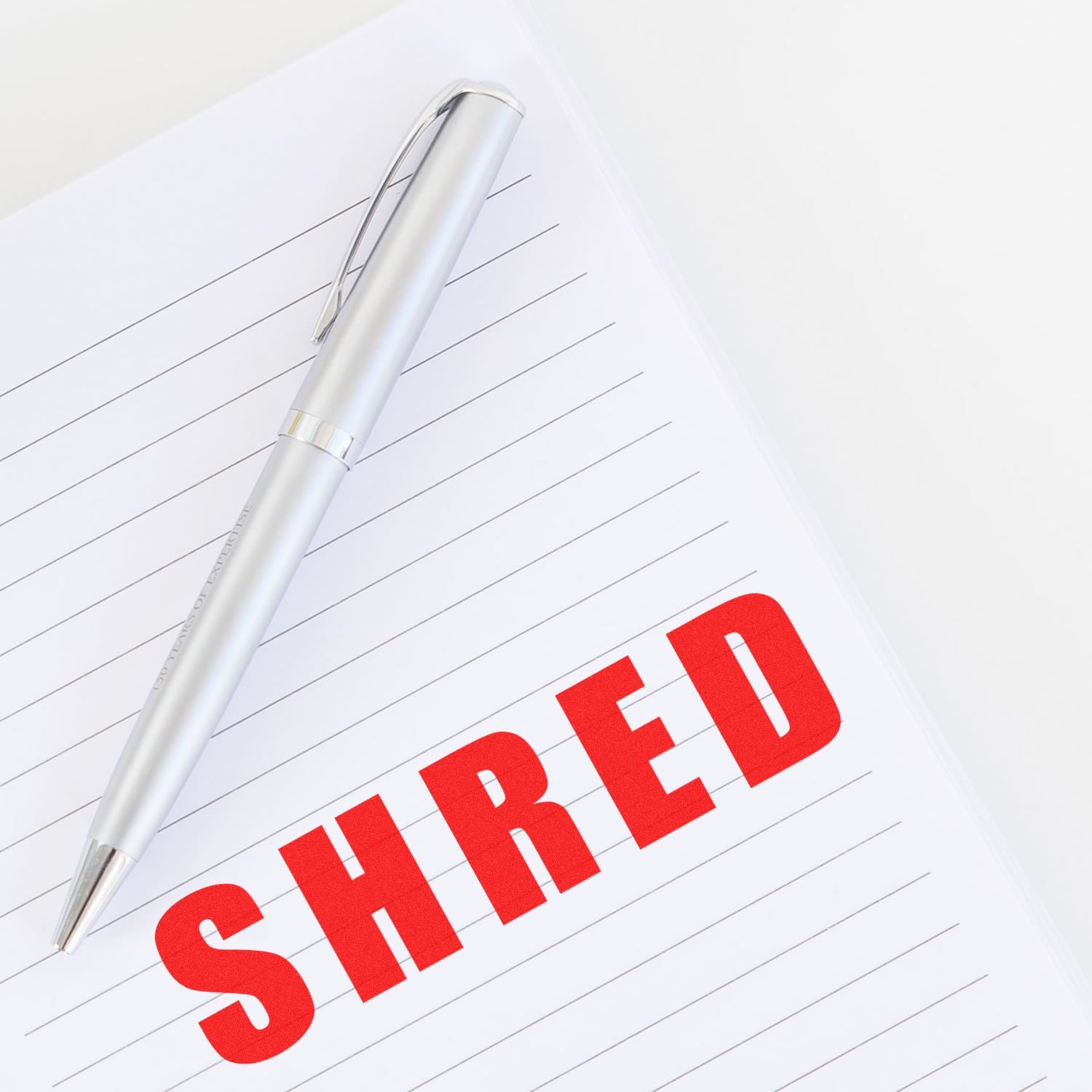 Silver pen on lined paper with bold red SHRED text, symbolizing document shredding and secure paper disposal.