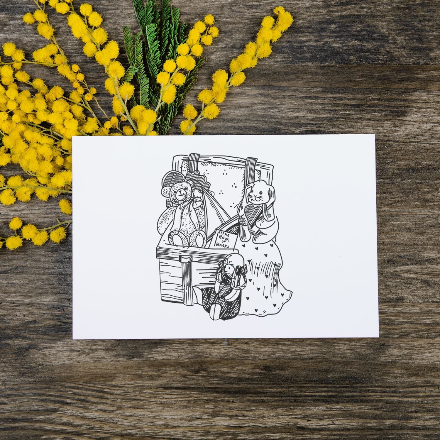 Teddy bear illustration card with yellow mimosa flowers on rustic wooden table.
