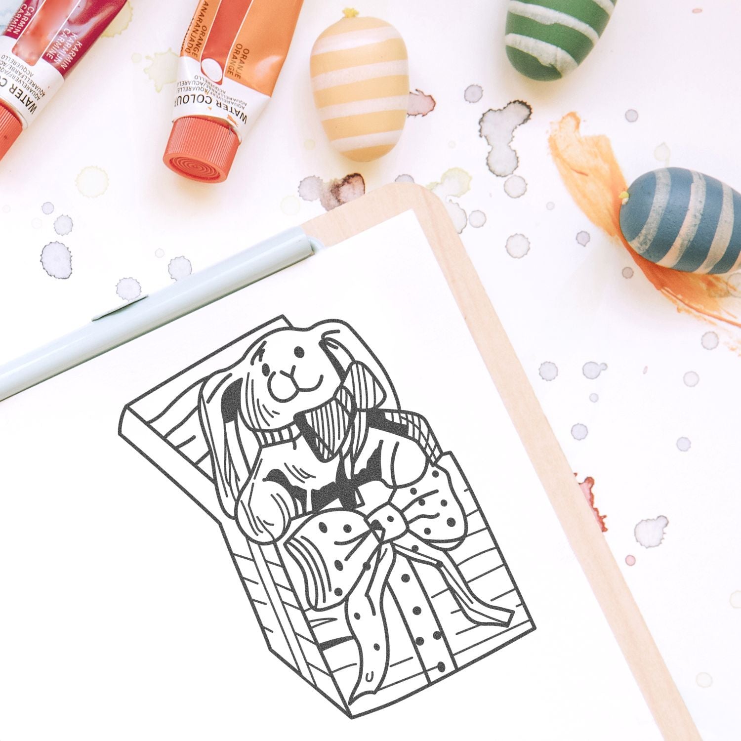 Easter bunny coloring page in a gift box with watercolor paints and painted eggs on a craft table