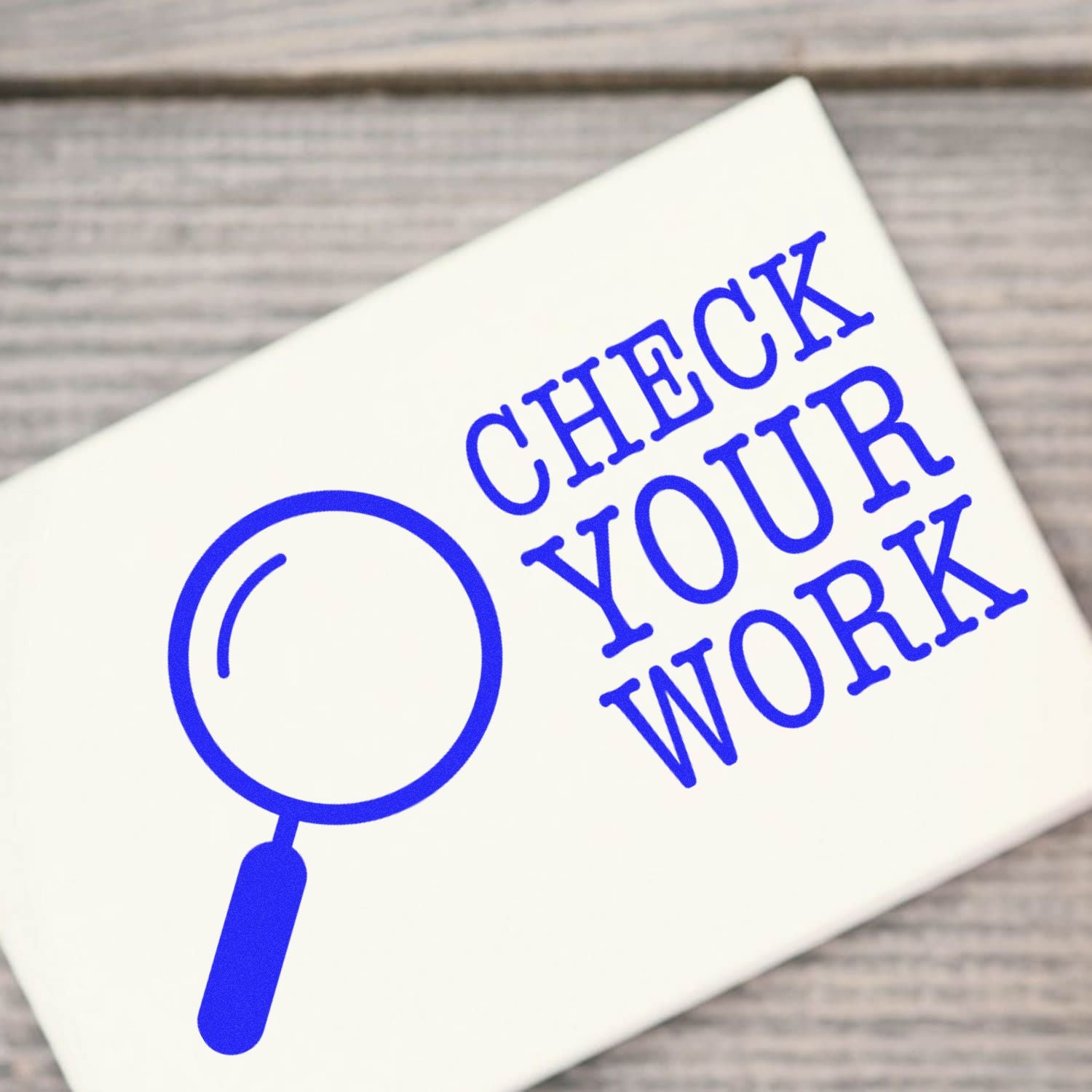 Close-up of a white card with a magnifying glass icon and blue Check Your Work text, symbolizing proofreading and quality review.