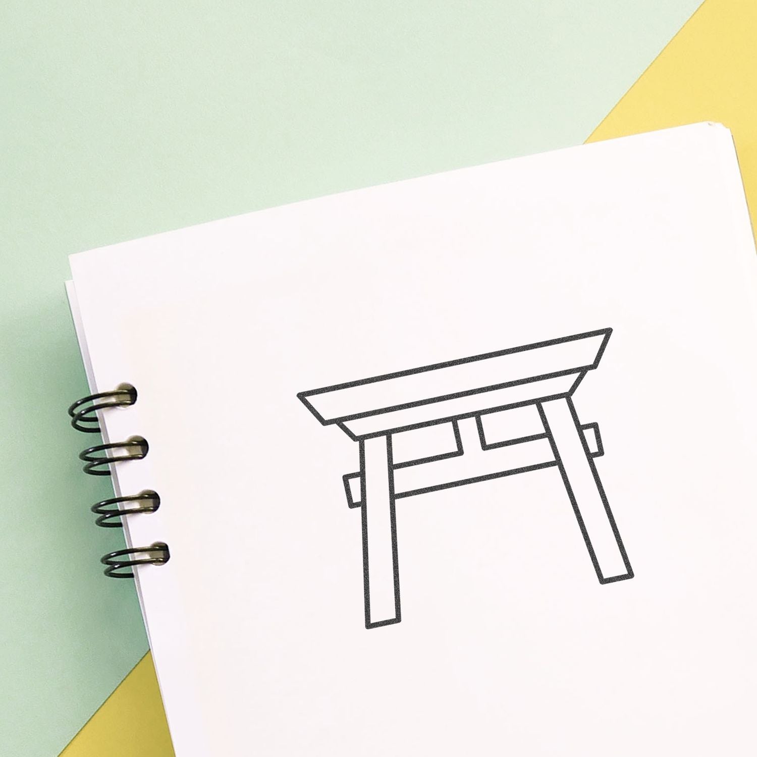 Minimal torii gate line drawing on a spiral notebook page with pastel background