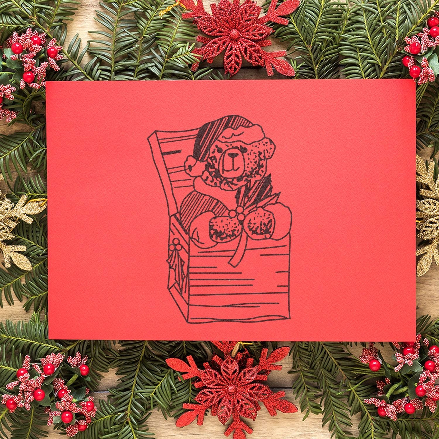 Red Christmas card with cute teddy bear in Santa hat on a festive pine and berry holiday background