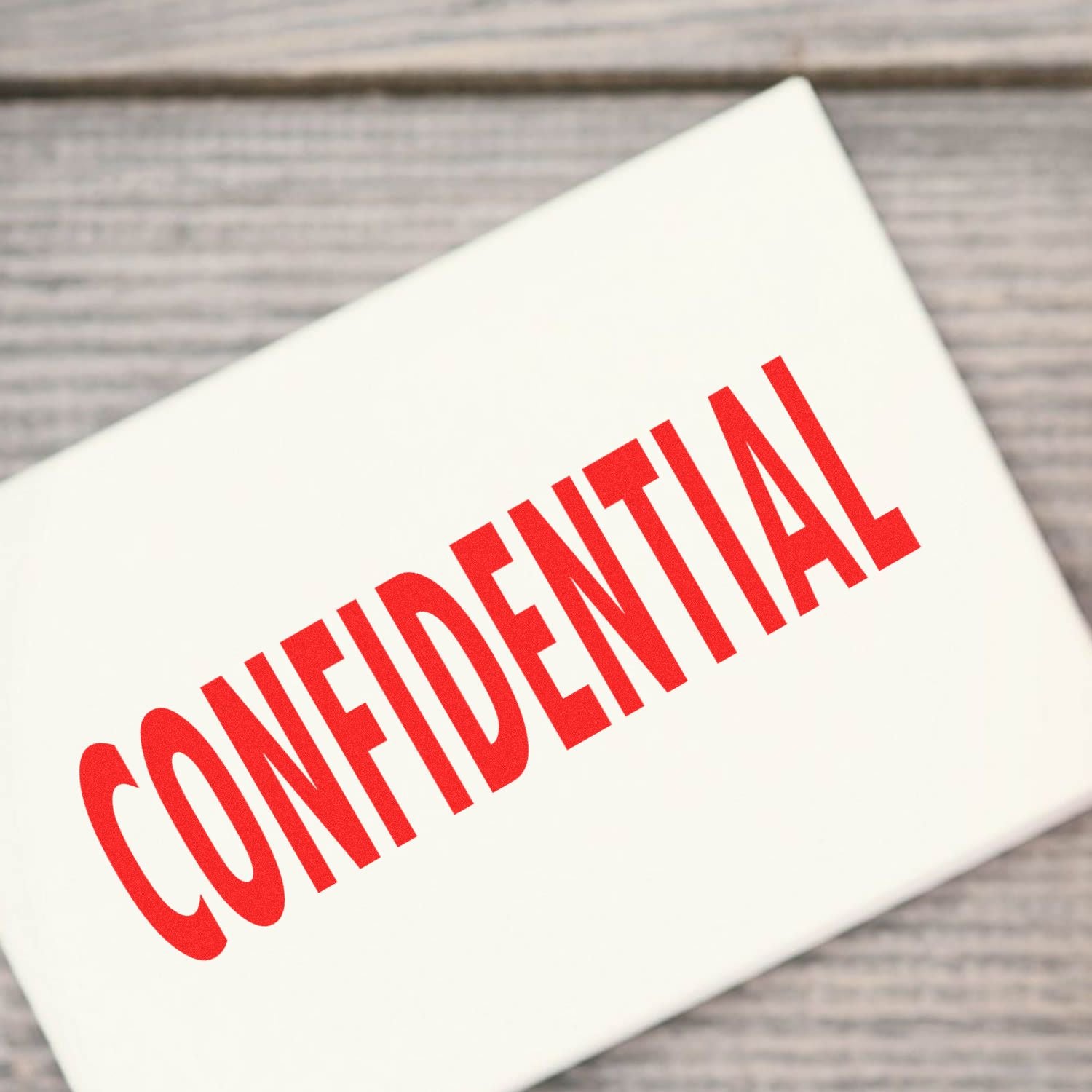 Red confidential stamp on white document envelope on a wooden background