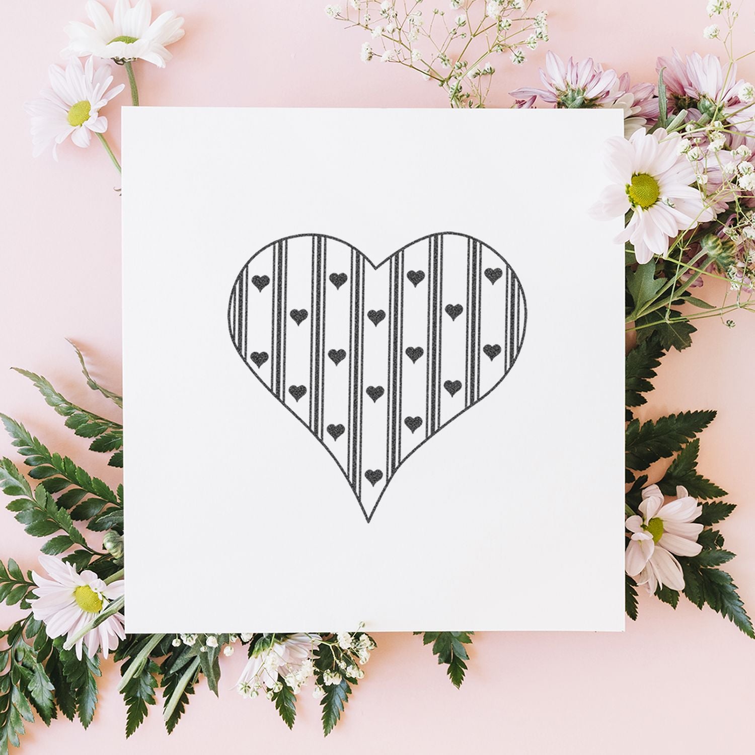 Minimalist black heart line art on white card surrounded by pink daisies and greenery on a pastel pink background.