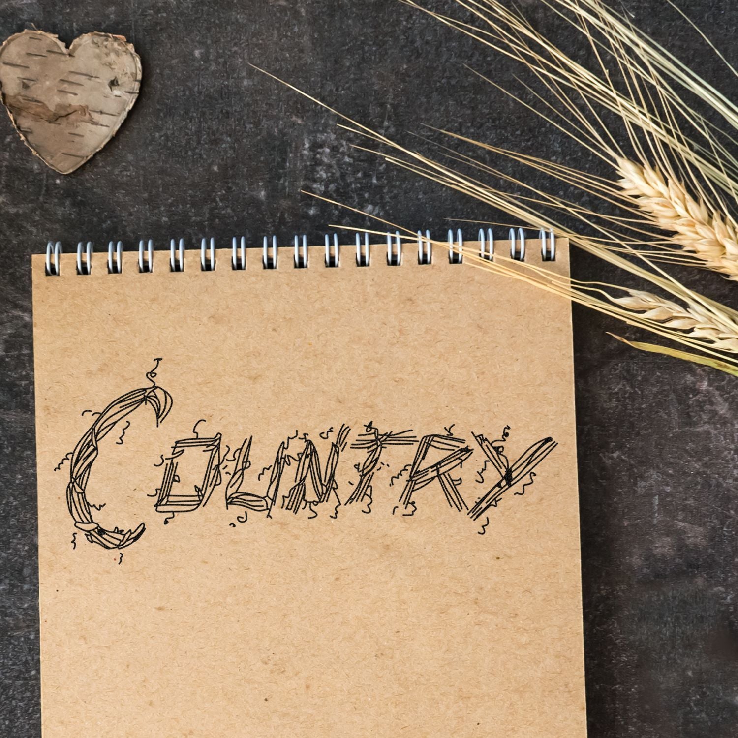 Rustic kraft paper notebook with hand-drawn lettering, wheat stalks, and a birch heart on a dark textured background.